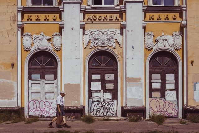 Typische Strassenbilder von Russland wie dieses mit einer weiss-gelben und klassisch verzierten Hauswand mit tags und einem älteren Herrn der davor lang geht sieht man wenn man das Land bereist.