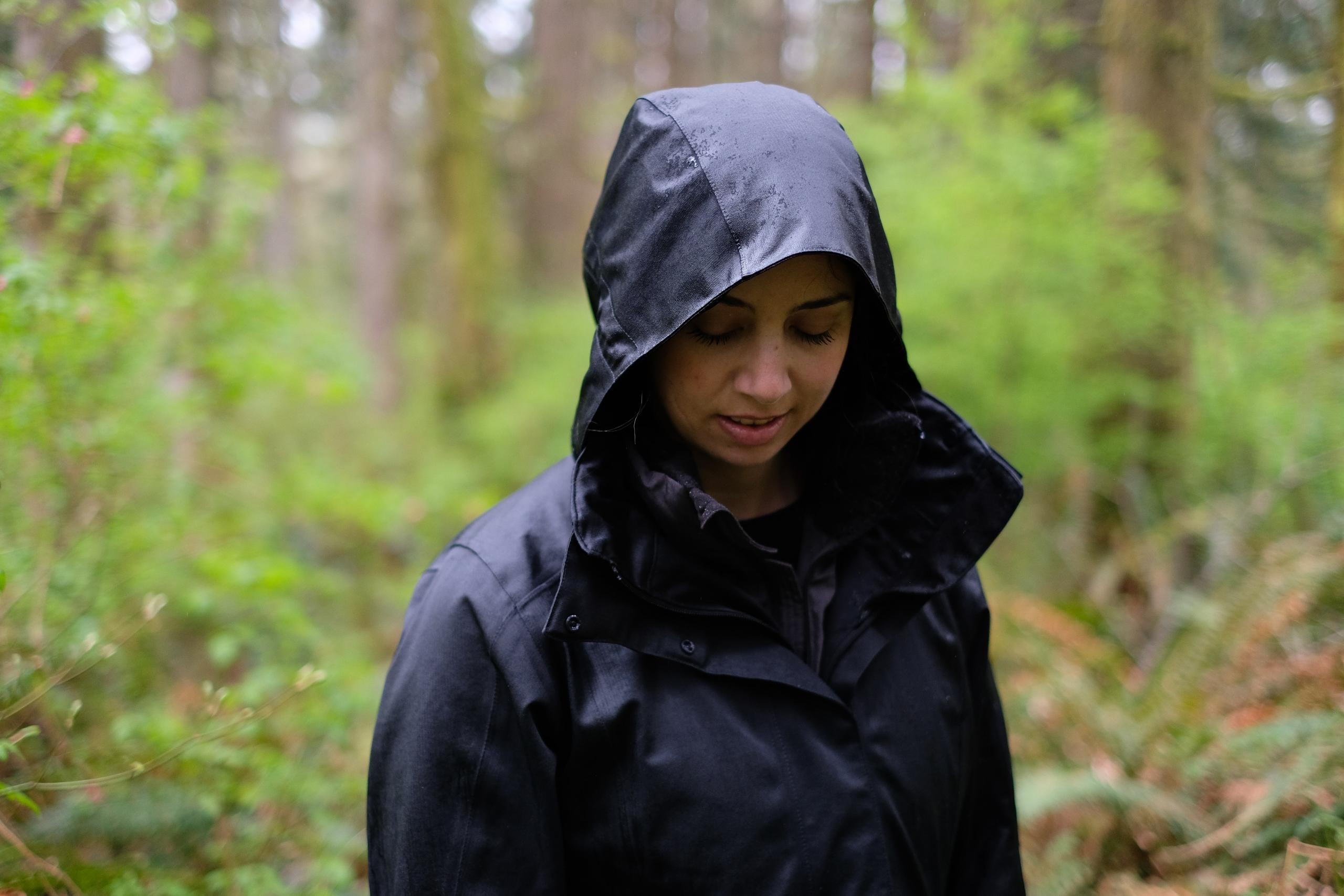 Die Frau hat die Kapuze ihrer Regenjacke hochgeschlagen und sie schaut nach unten. 
