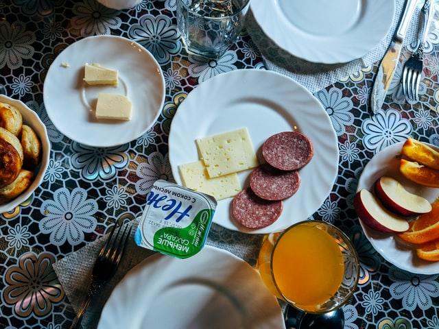Ein russisches Frühstück das aus Obst und tierischen Produkten besteht steht auf einem Tisch mit einer weissen Häkeldecke.