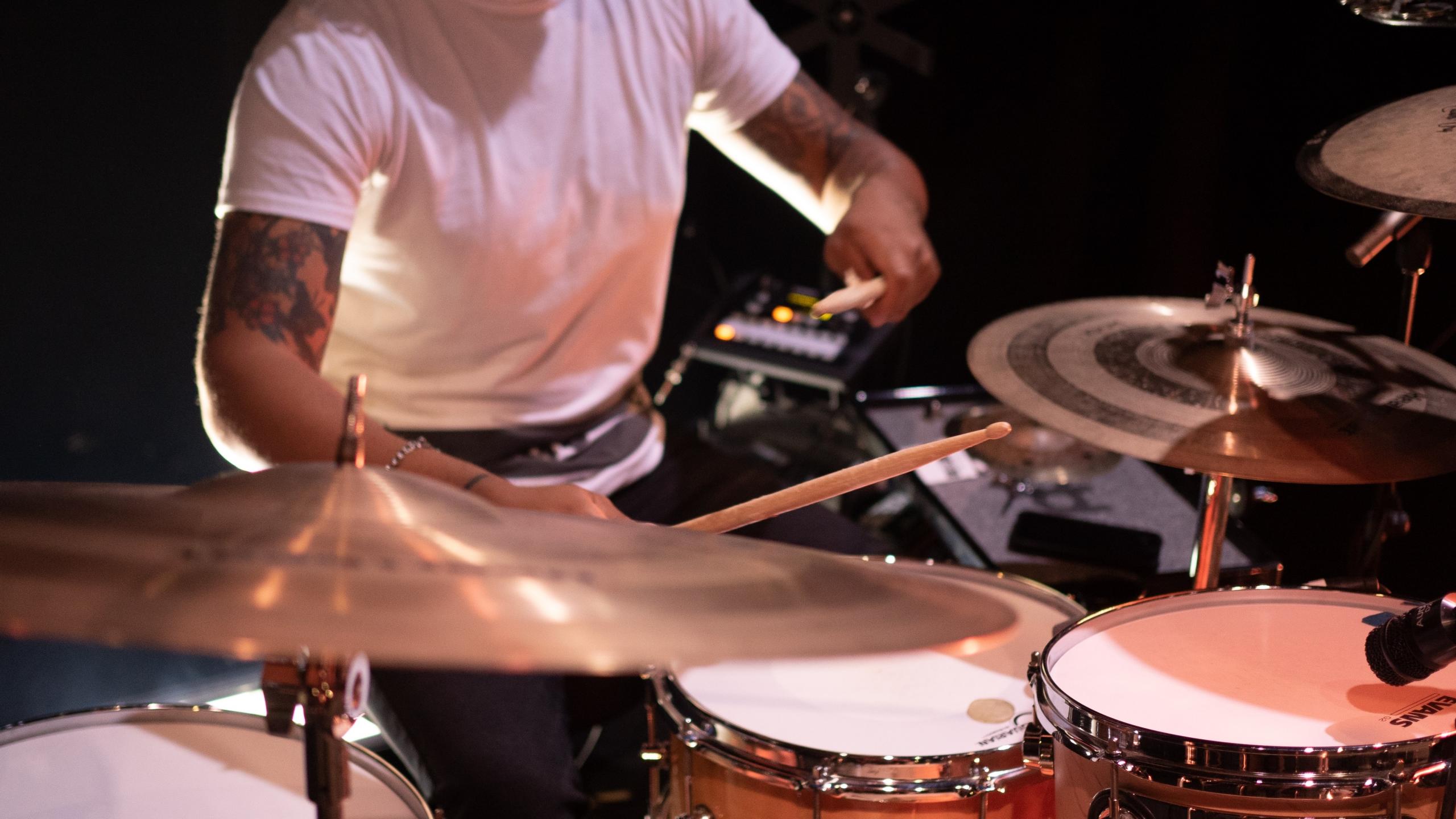 Ein Schlagzeuger in weißem T-Shirt spielt auf seinem mikrofonierten Drum-Set.