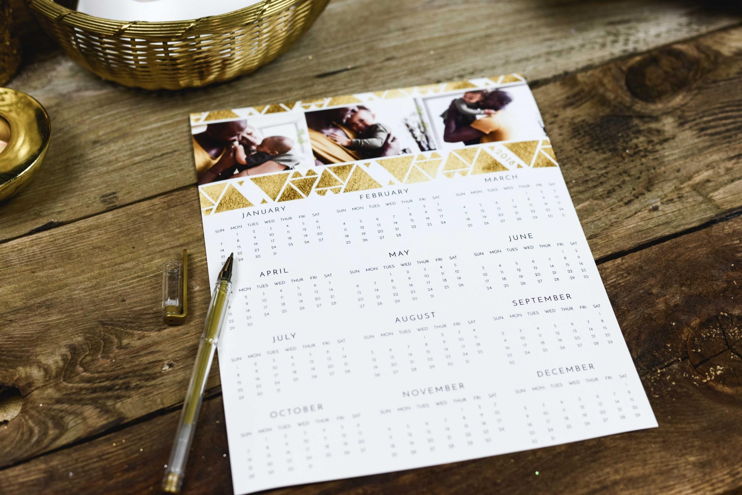Auf einem Holztisch liegen ein Jahreskalender und ein geöffneter Kugelschreiber.