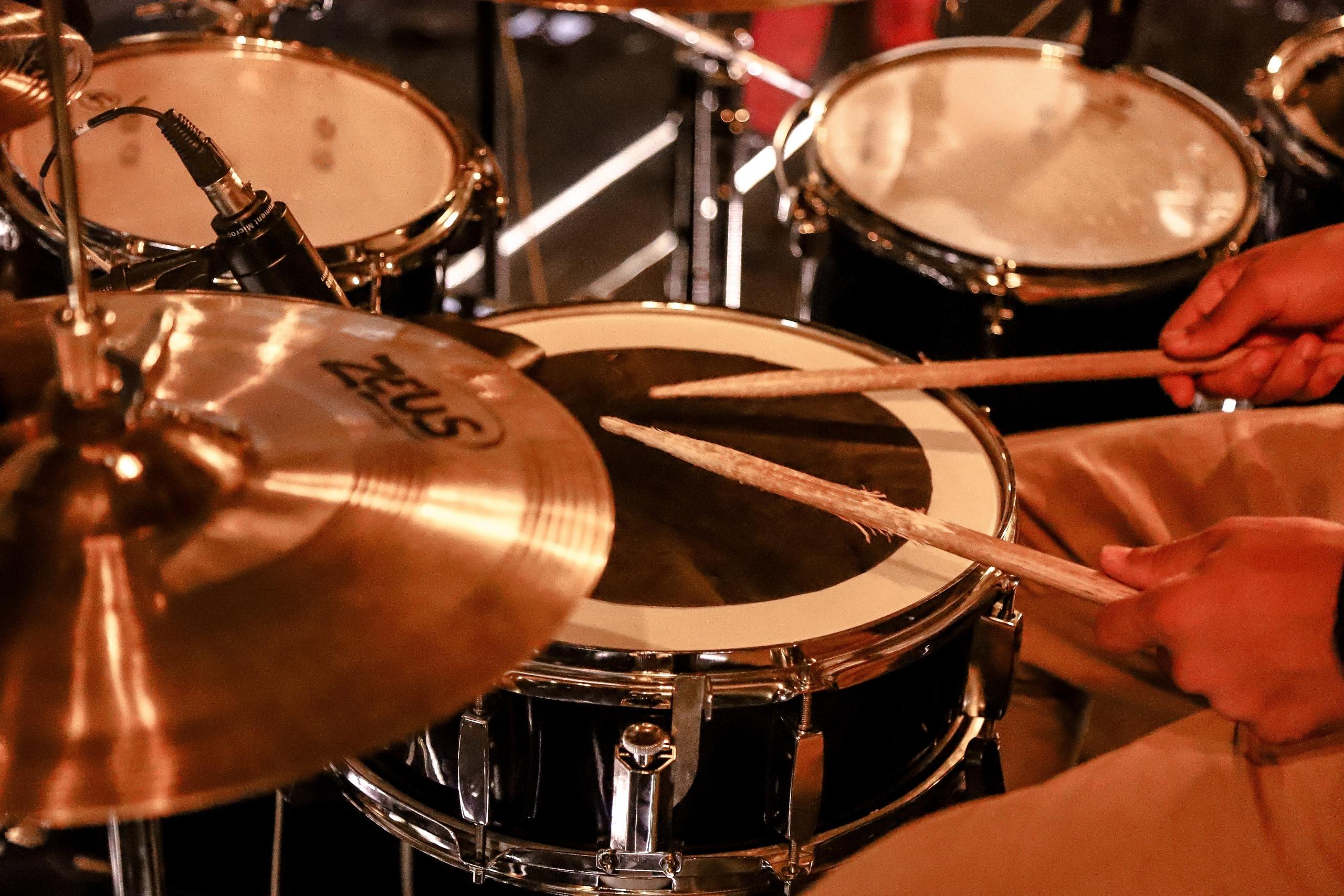 Die schon leicht abgenutzten Drum-Sticks spielen die Snare und daneben stehen Becken und Toms.