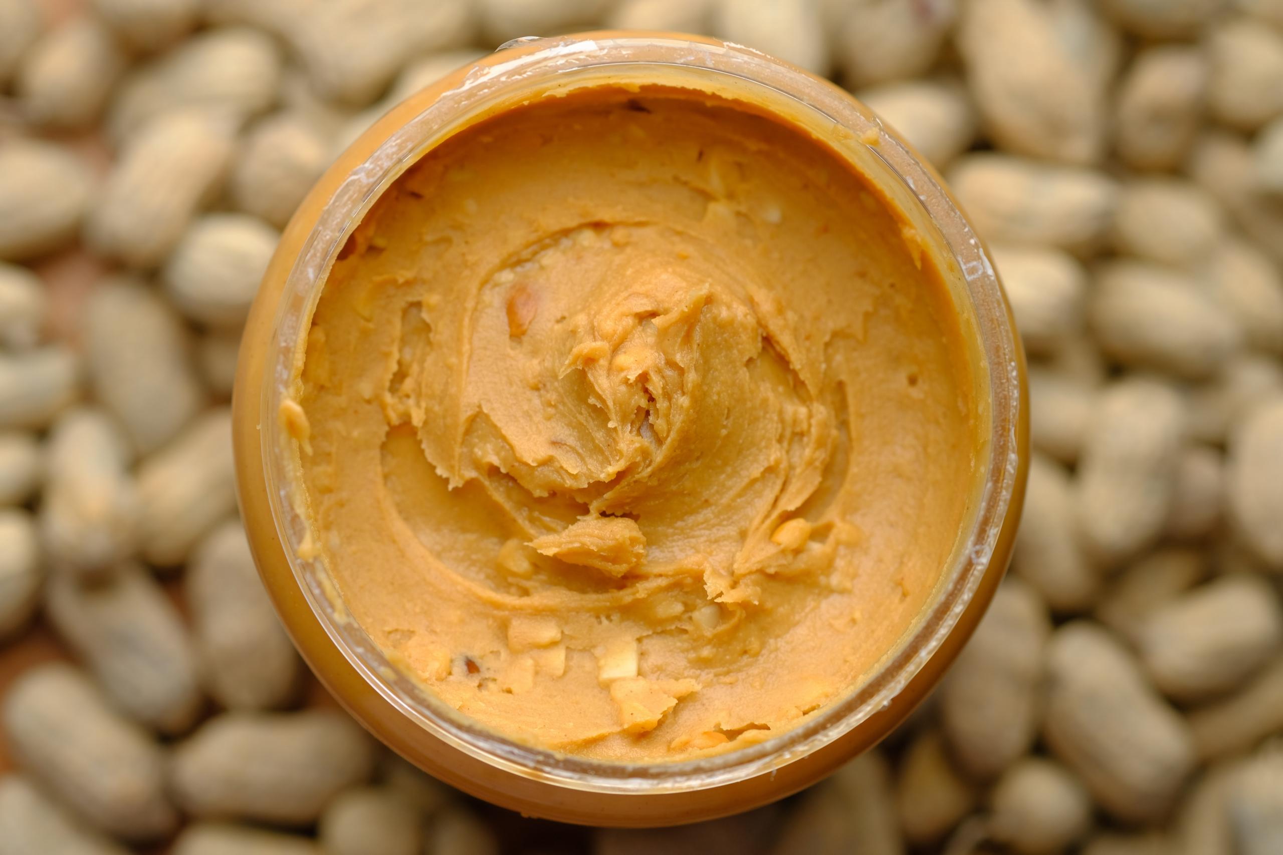 Auf einem Haufen ungeschälter Erdnüssen steht ein volles Glas Erdnussbutter.