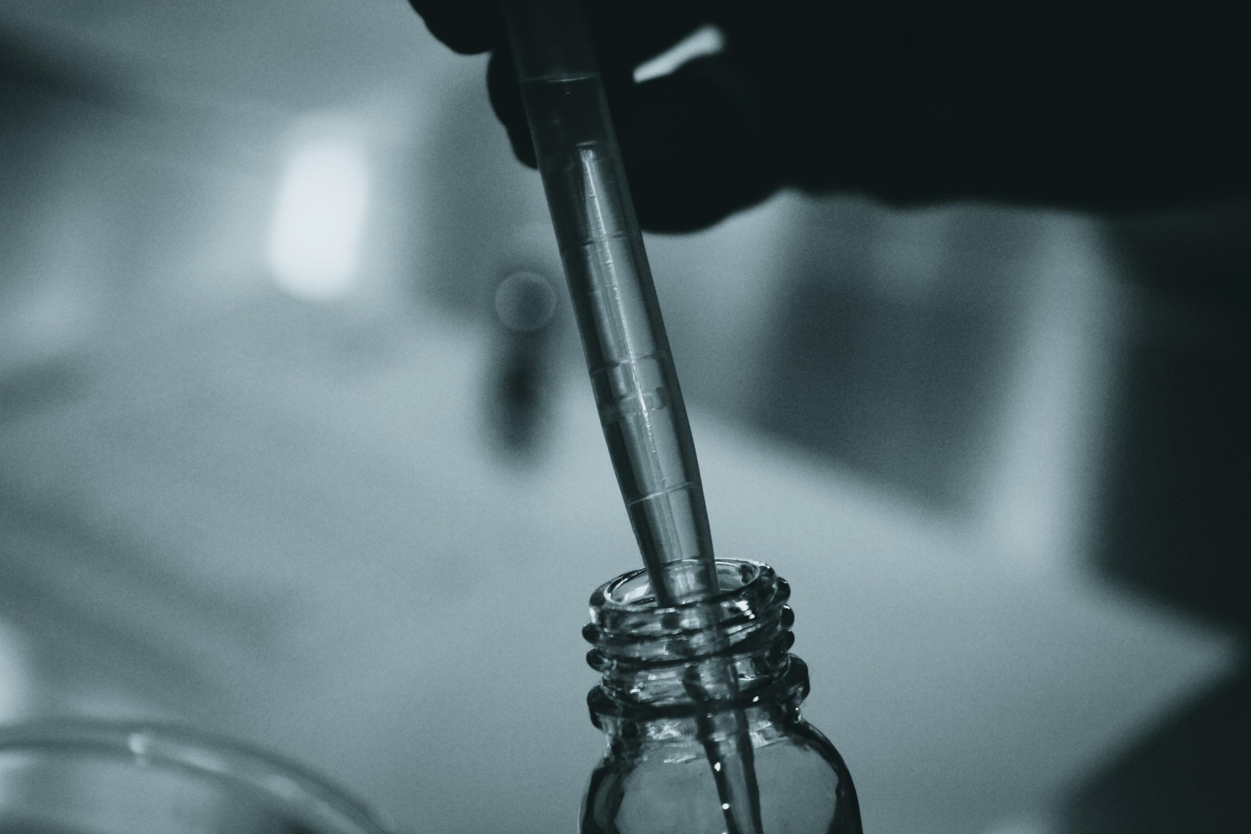 Eine Pipette wird behutsam in ein kleines Glassgefäss eingetaucht.
