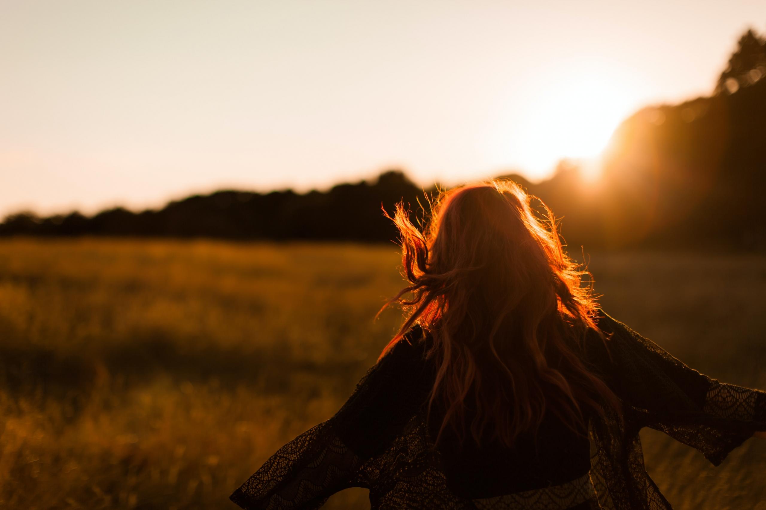 Eine Person mit langen Haaren rennt über ein Feld der untergehenden Sonne entgegen.