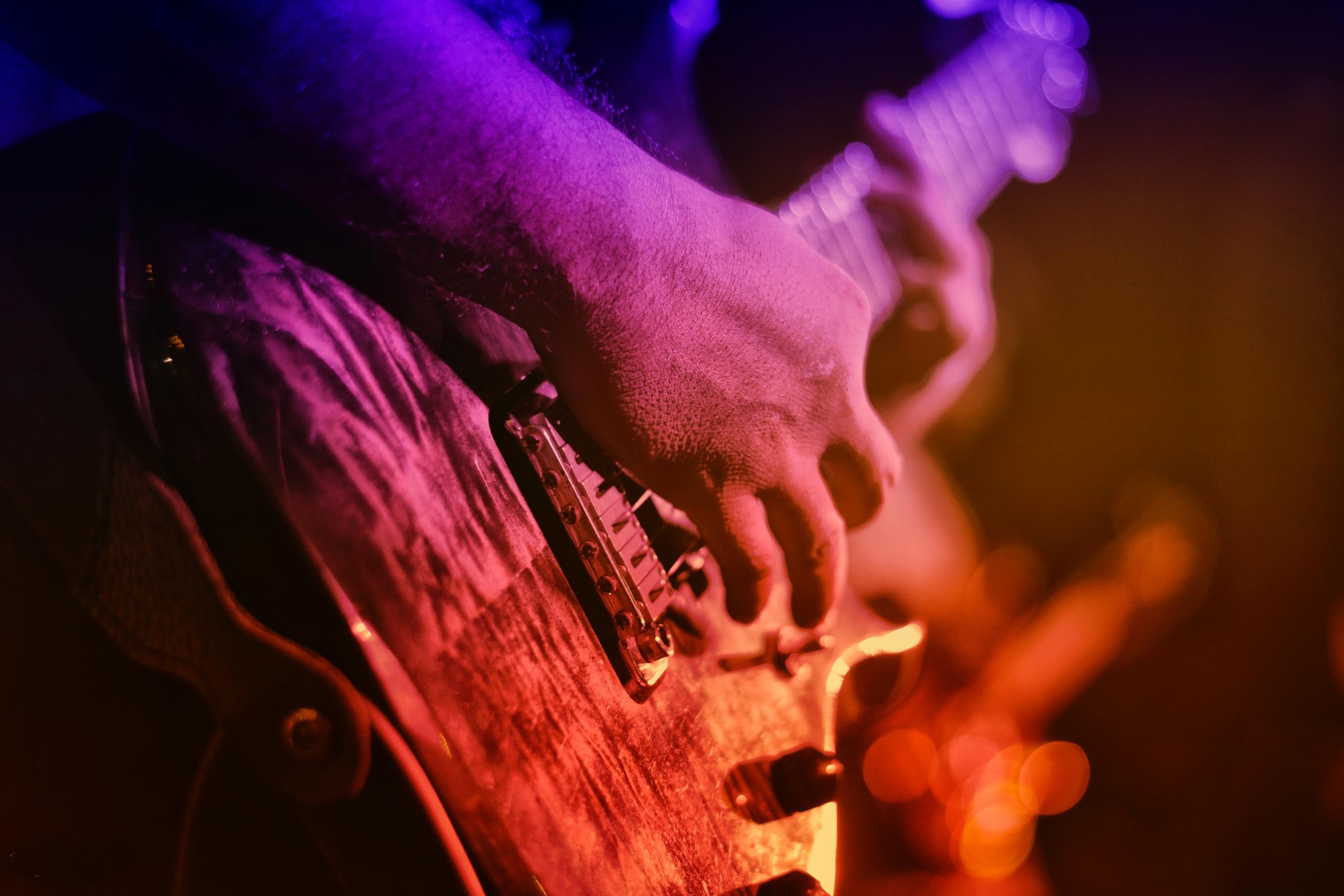 Der Korpus der E-Gitarre und die Schlaghand des Gitarristen sind im Vordergrund des Bildes.