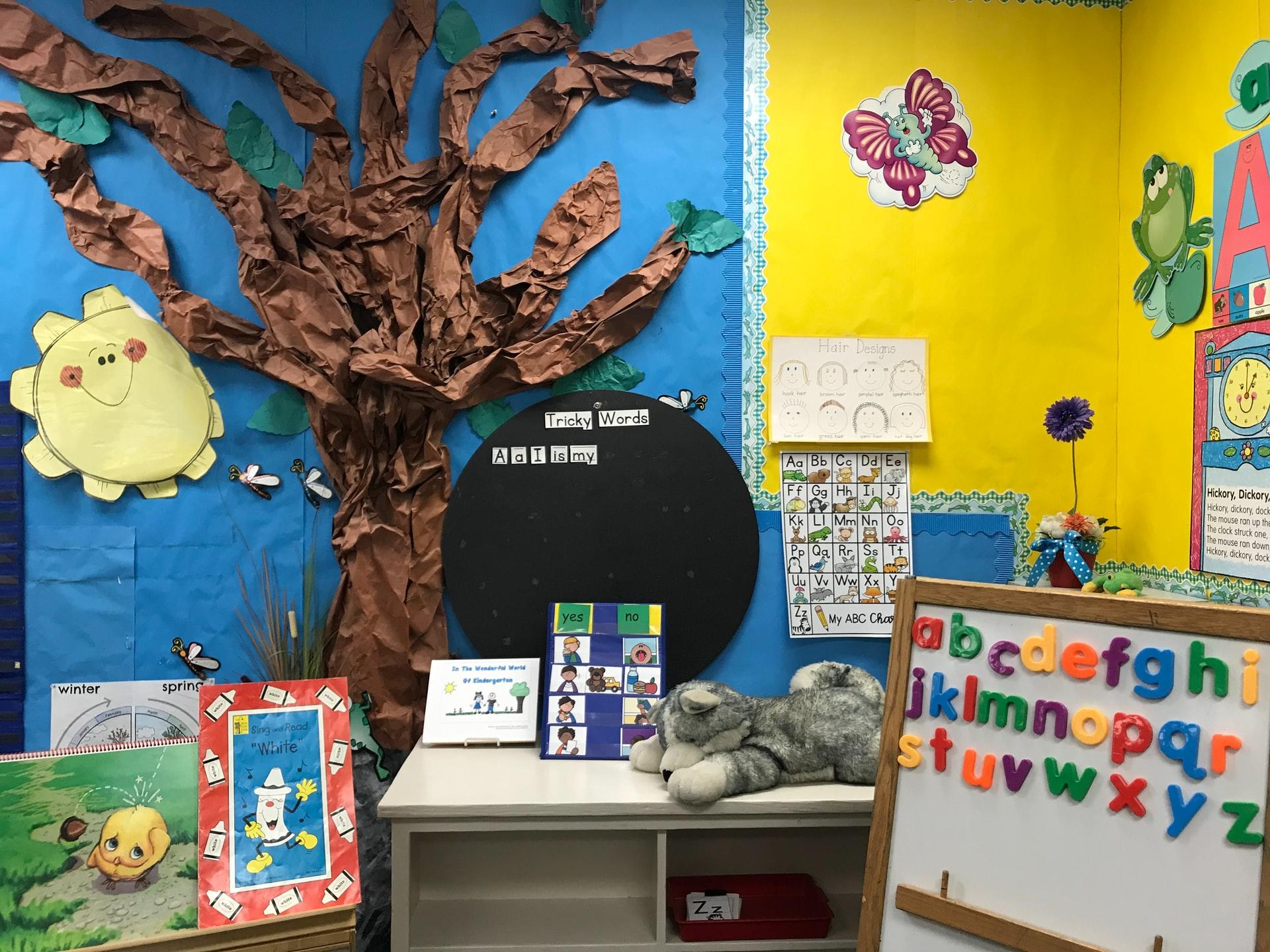 Ein bunt dekoriertest Klassenzimmer in der Grundschule mit einem gebastelten Baum auf einer blauen Wand und Lernmaterialien im Vordergrund