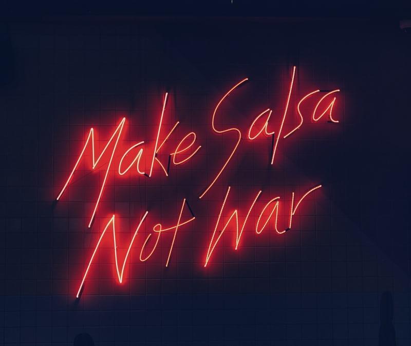 Make Salsa, not War steht in roter Neon-Leuchtschrift auf schwarzem Untergrund.