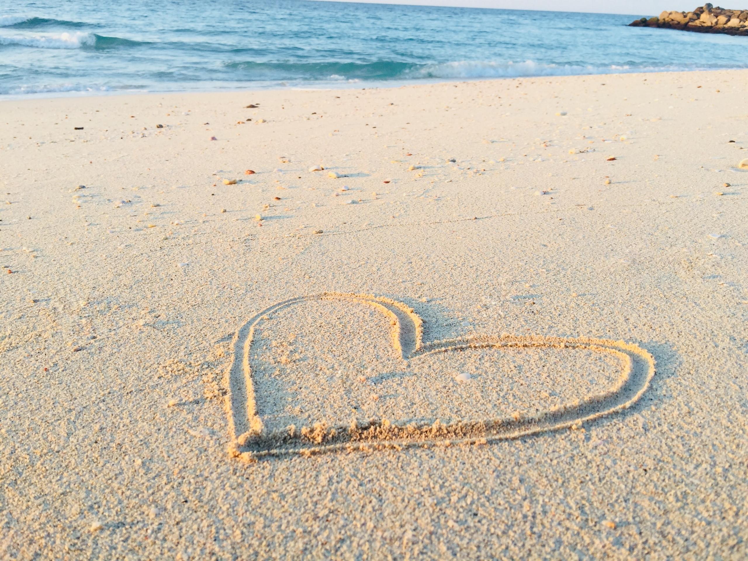 Ein Herz im Sand, das Meer im Hintergrund