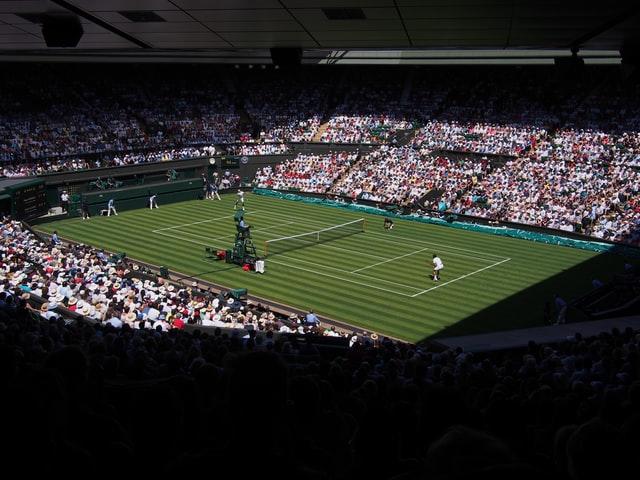 Ein mit Zuschauern gefülltes Tennis Stadion mit Rasen ist aus der Perspektive von schräg oben fotografiert.