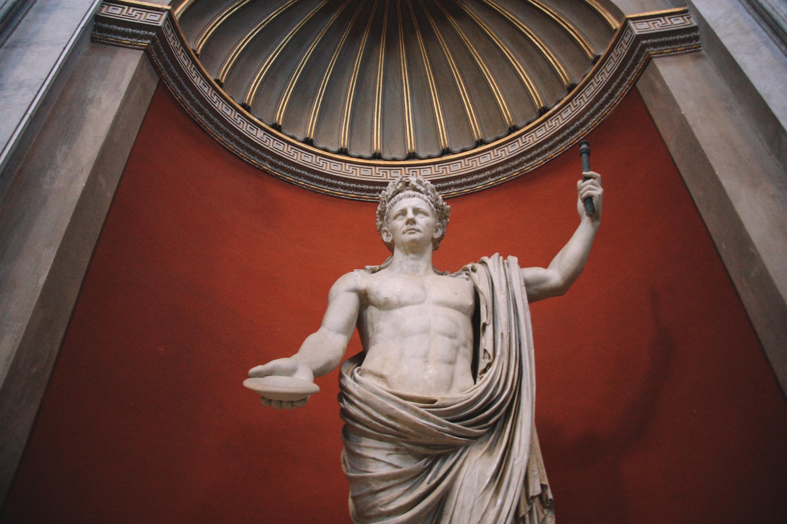 Eine Marmorstatue mit Dornenkranz steht vor einem roten Hintergrund, der einer Kapelle gleicht.
