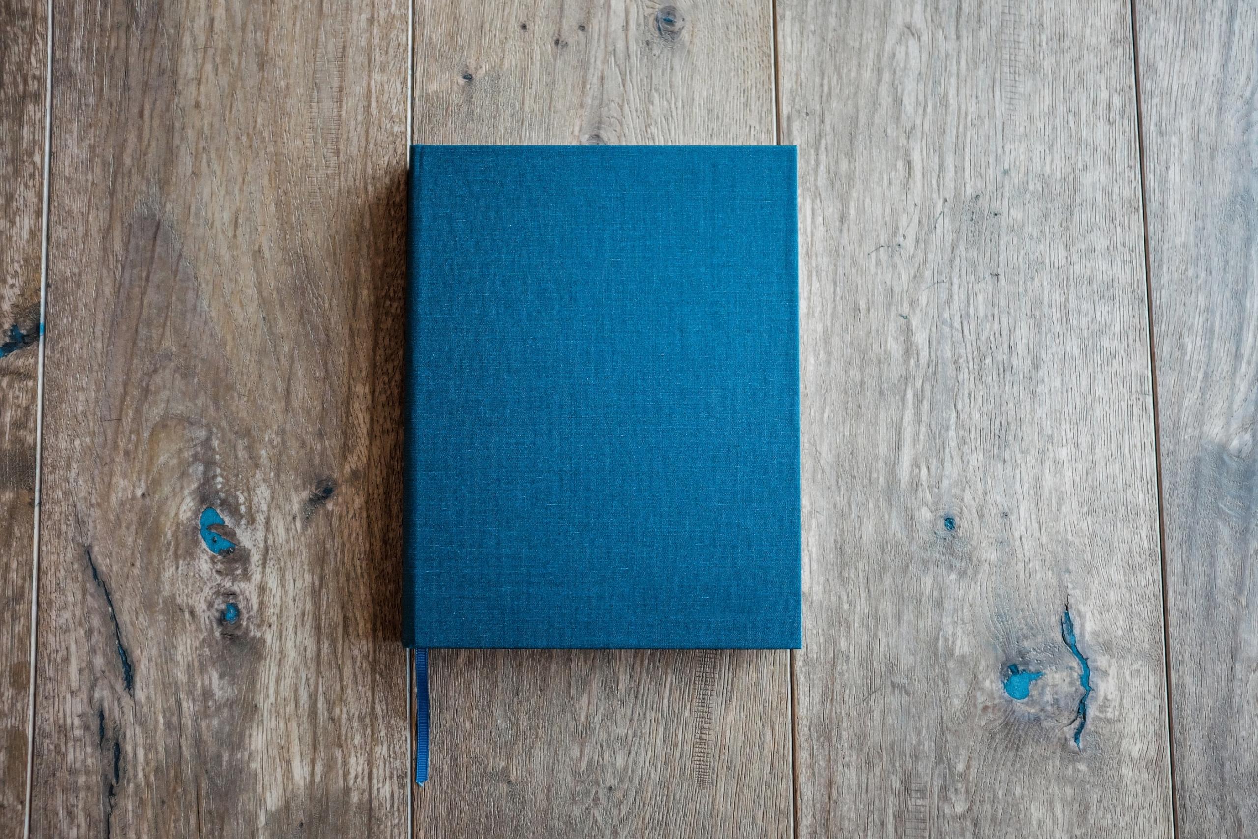 Auf dem Holzboden liegt ein geschlossenes Buch mit dunkelblauem Einband.