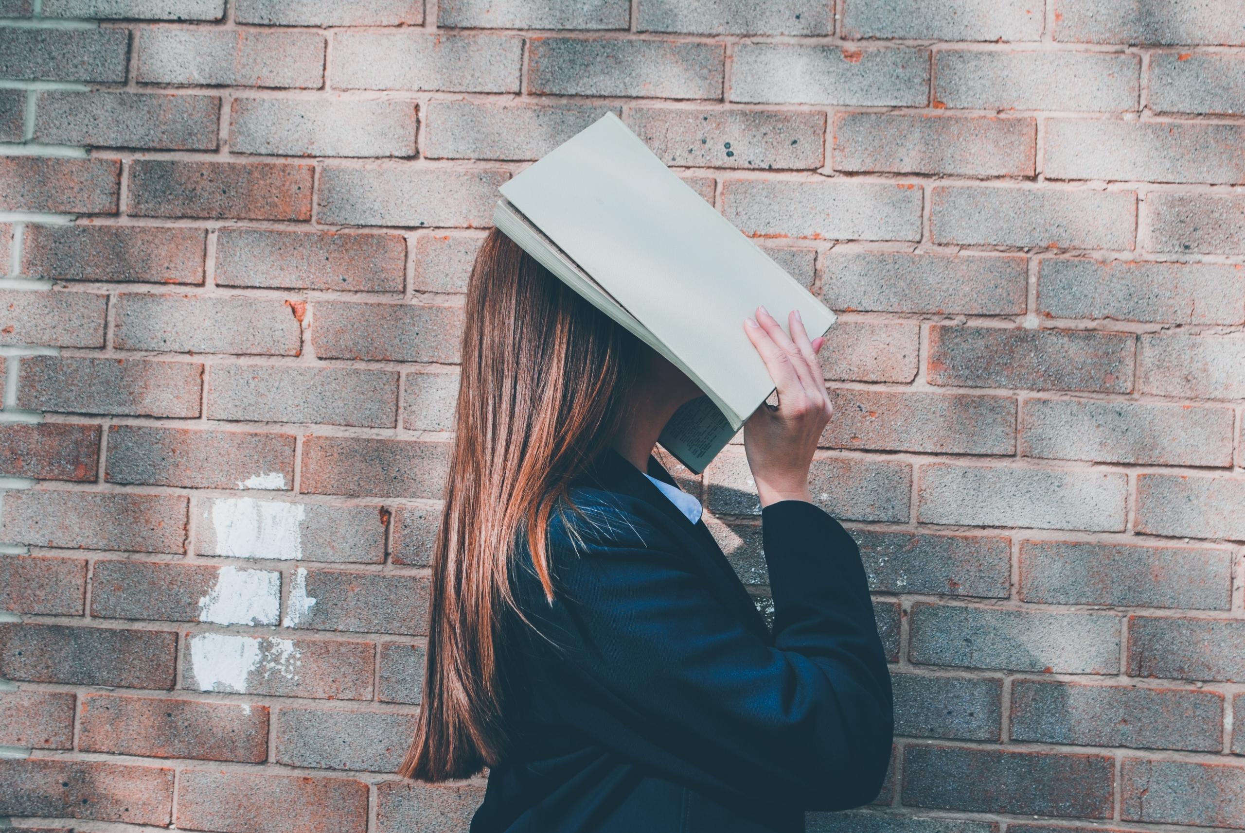 Eine Frau schaut nach oben und legt sich ein offenes Buch aufs Gesicht.