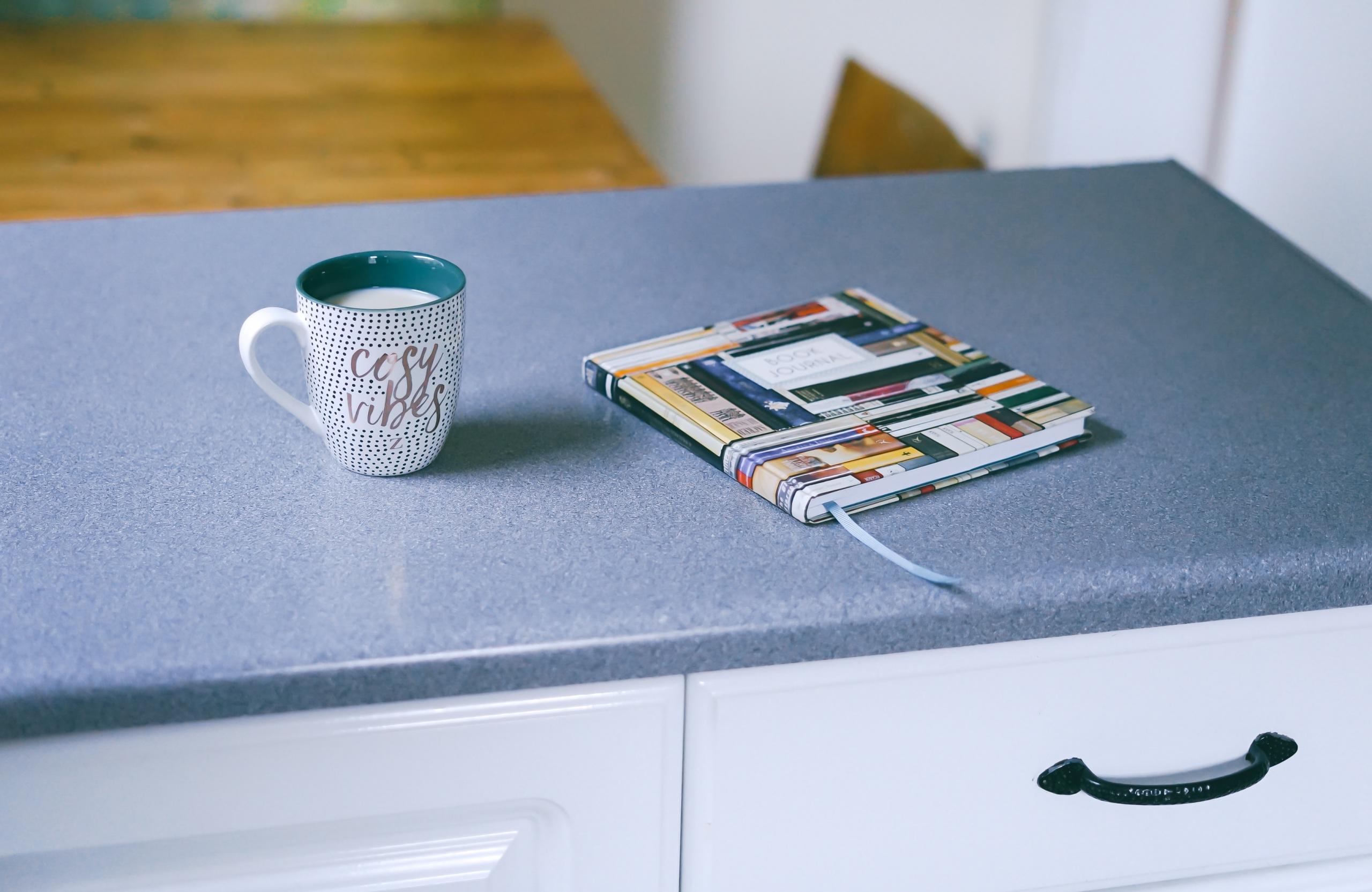 Auf einer Ablage mit Schublade steht eine Tasse Milch neben einem bunten Buch.