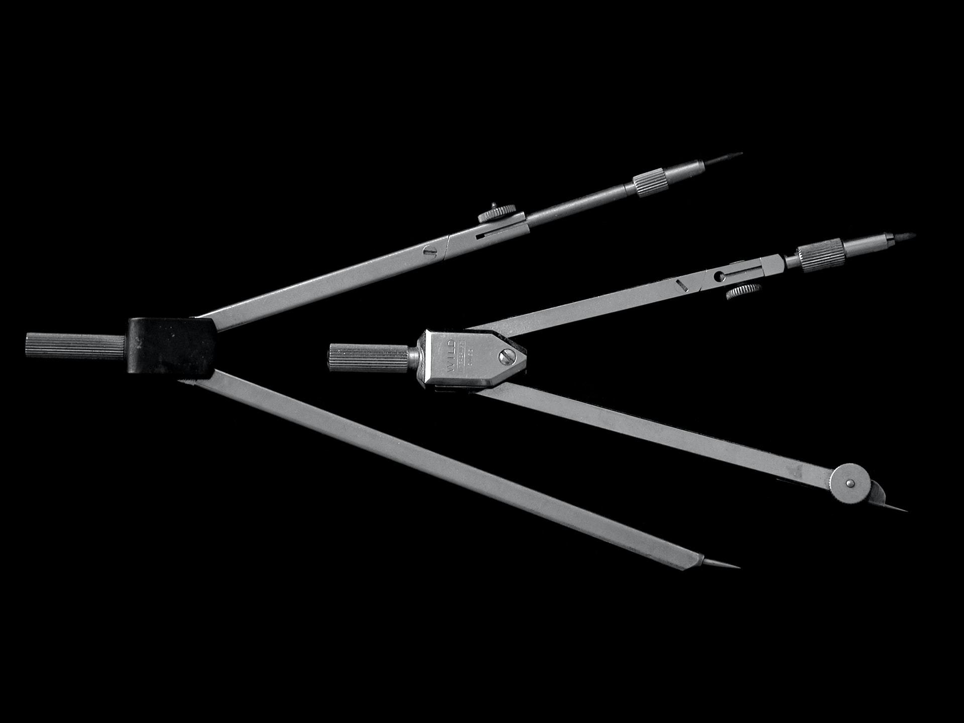 Auf einem schwarzen Untergrund liegen zwei silberne Zirkel ineinander gelegt