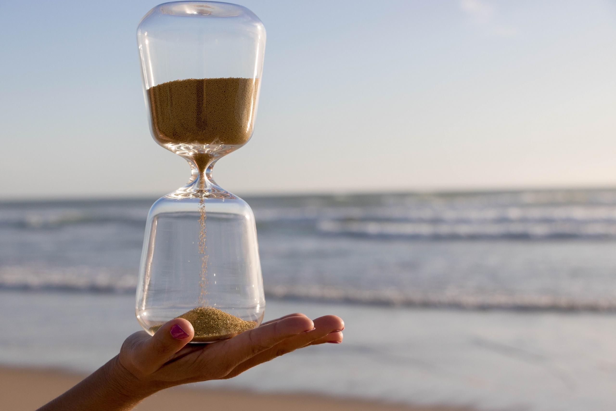 Eine Sanduhr läuft vor der Kulisse eines Meeres langsam ab.