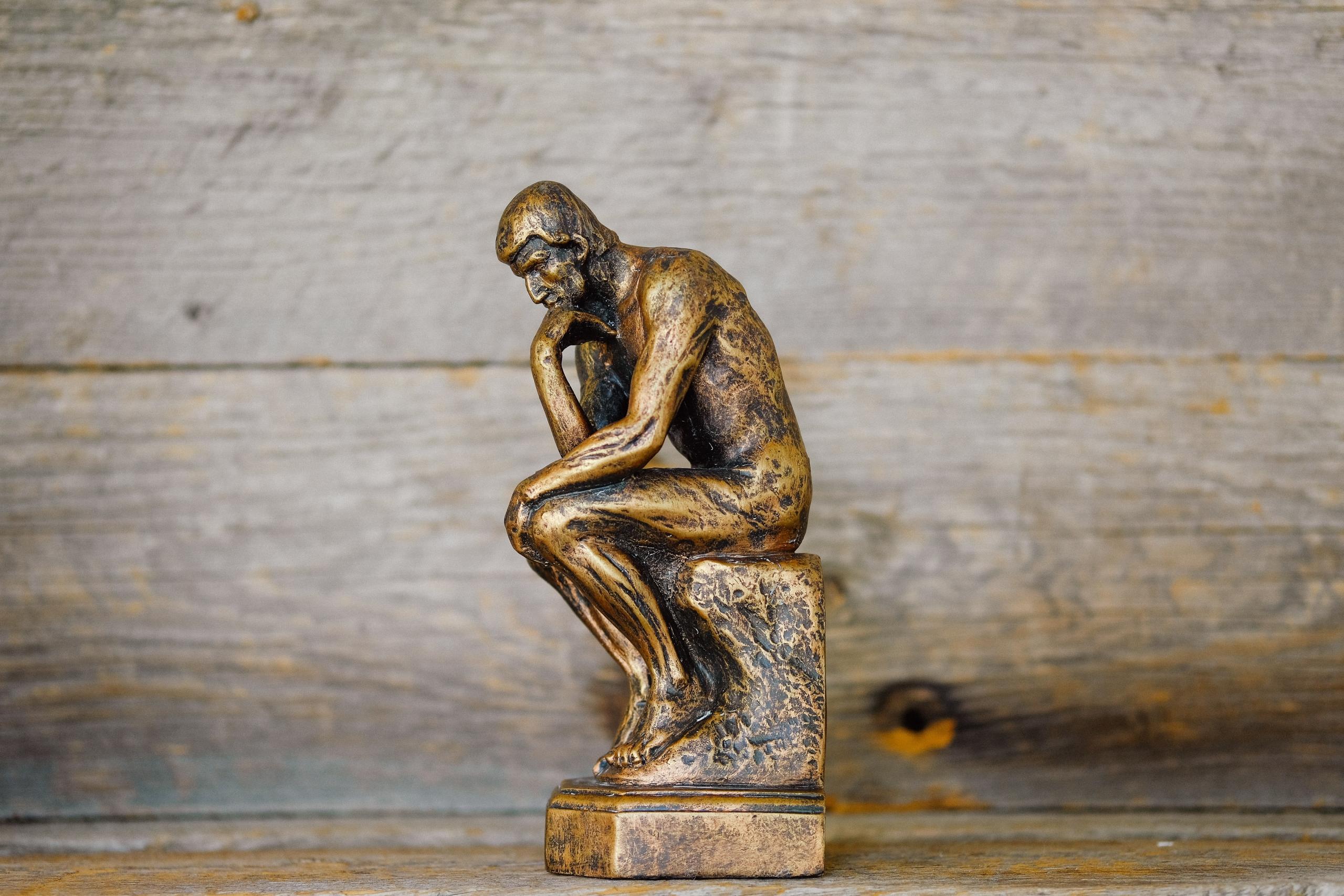 Rodins Denker als Miniaturstatue steht vor einem Holzhintergrund.