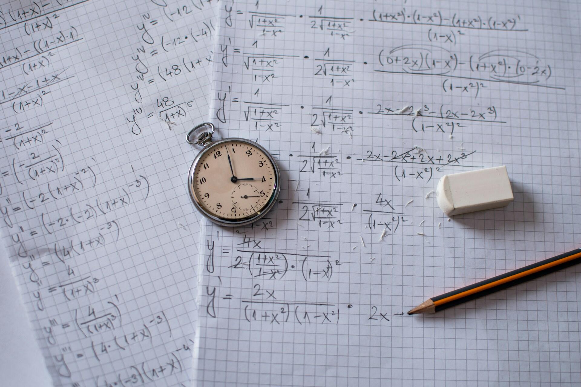 Taschenuhr und Stift liegen auf Blatt mit mathematischen Formeln.