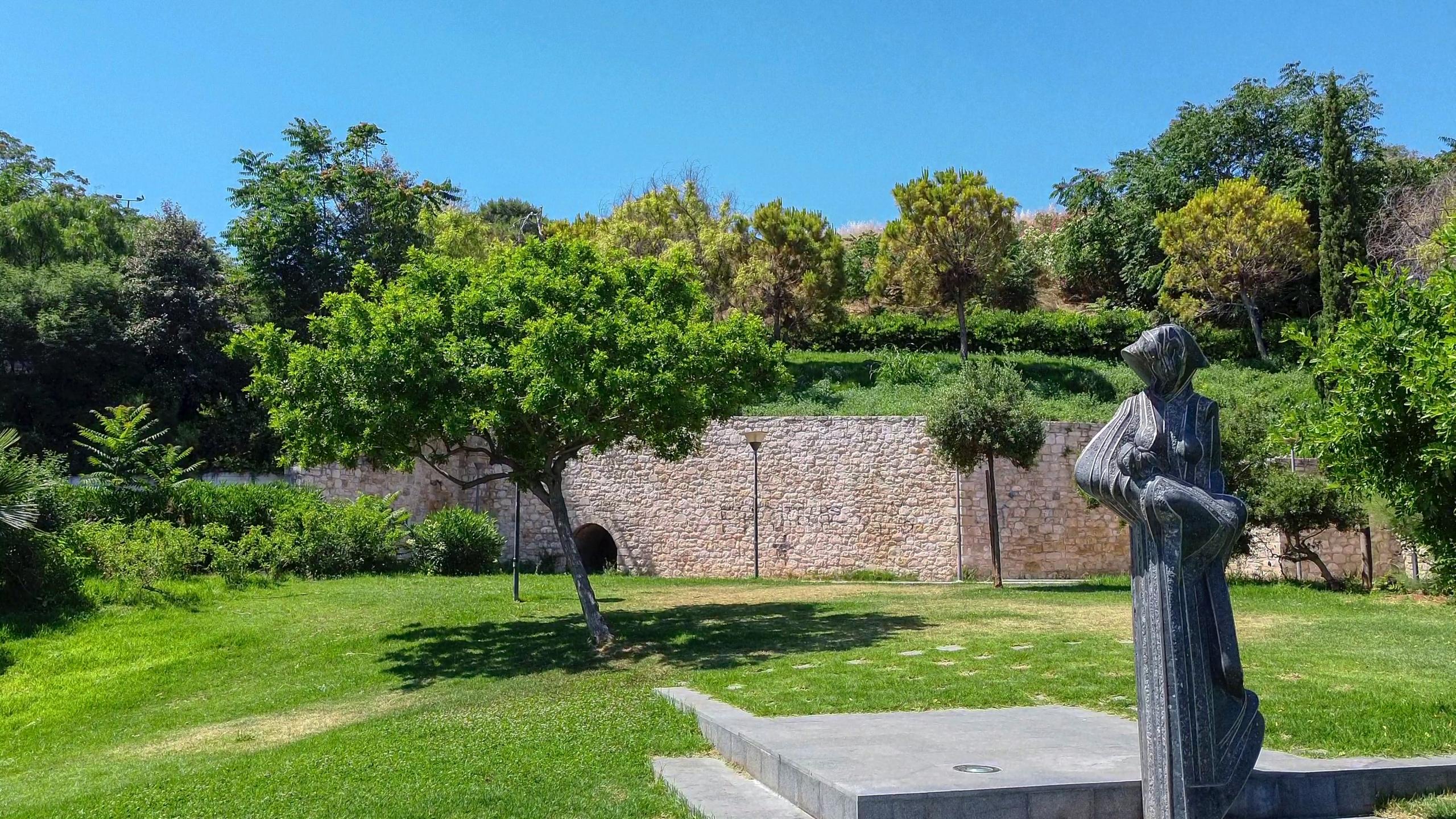 Ein grüner, bewachsener Garten erstreckt sich, im Vordergrund ist die Statue einer Frau.