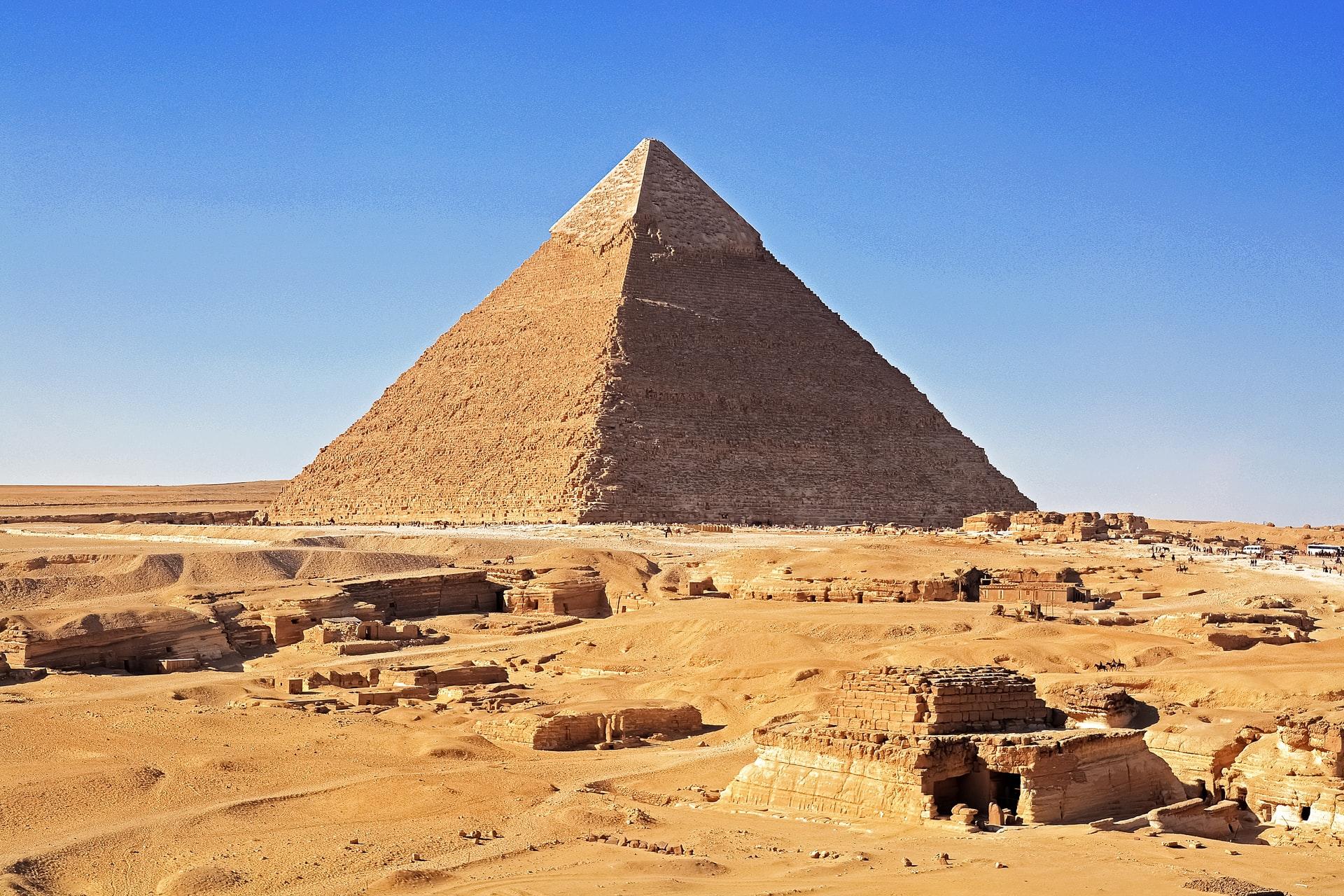 Eine antike Pyramide in der Wüste mit goldgelbem Sand im Vordergrund und einem strahlend blauen Himmel