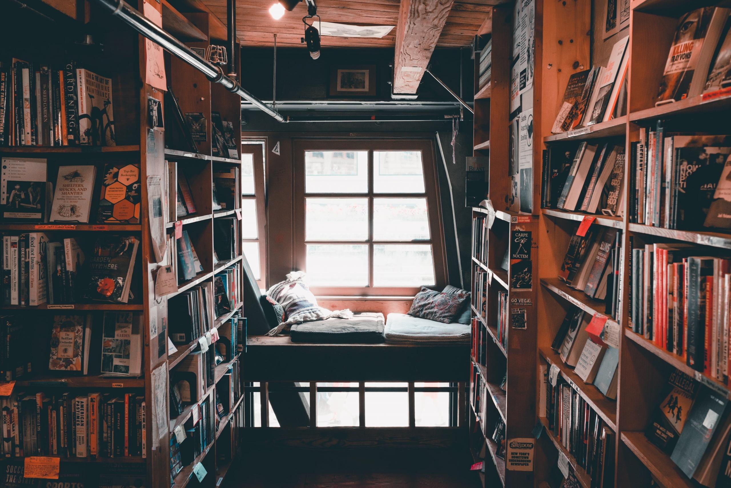 Eine Leseecke befindet sich am Fenster in einem Raum voller Bücher. Die Bücherregale zieren alle Wände des Raumes.