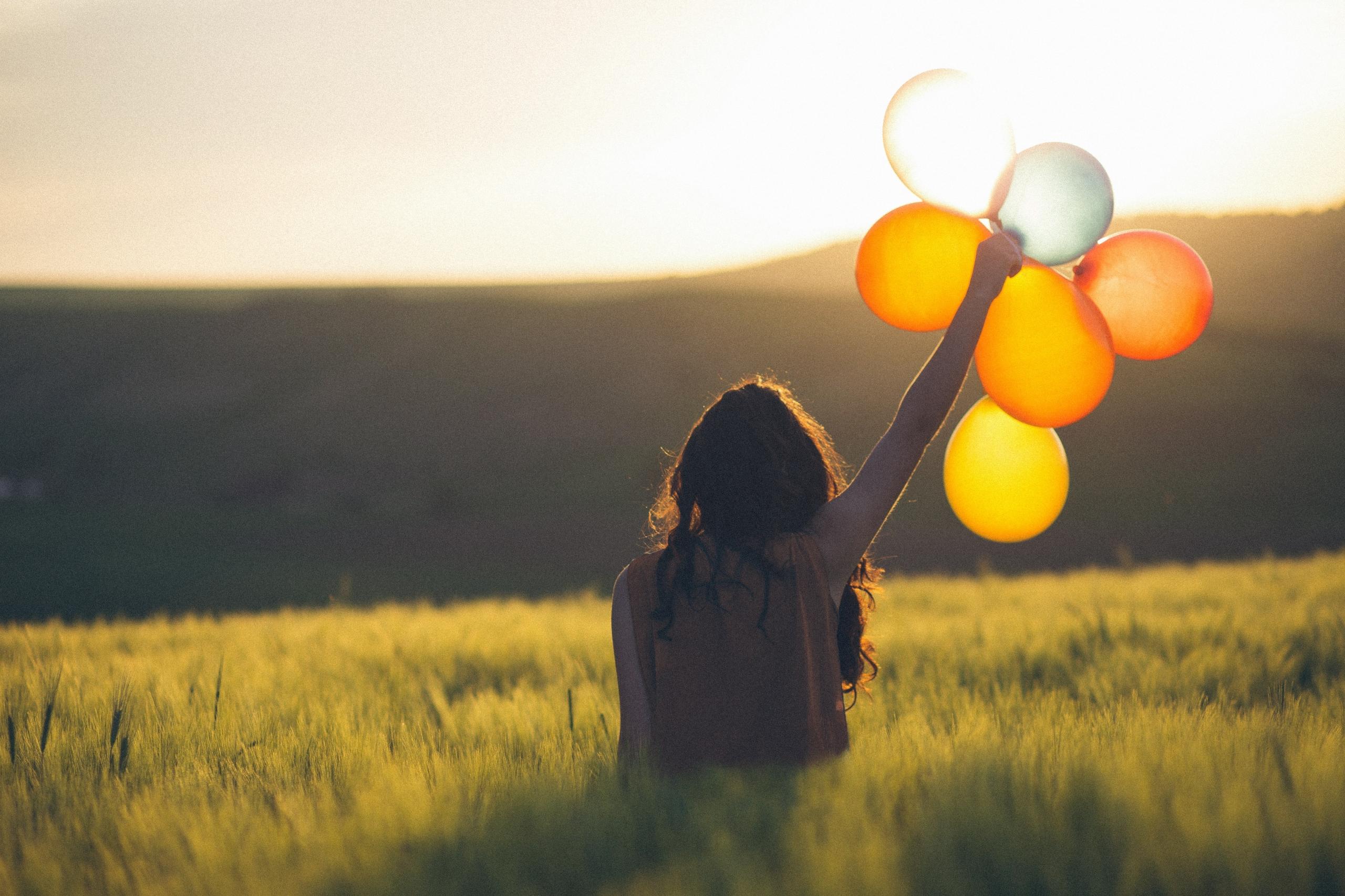 Eine Frau sitzt in einem Weizenfeld mit Luftballons und schaut der Sonne entgegen