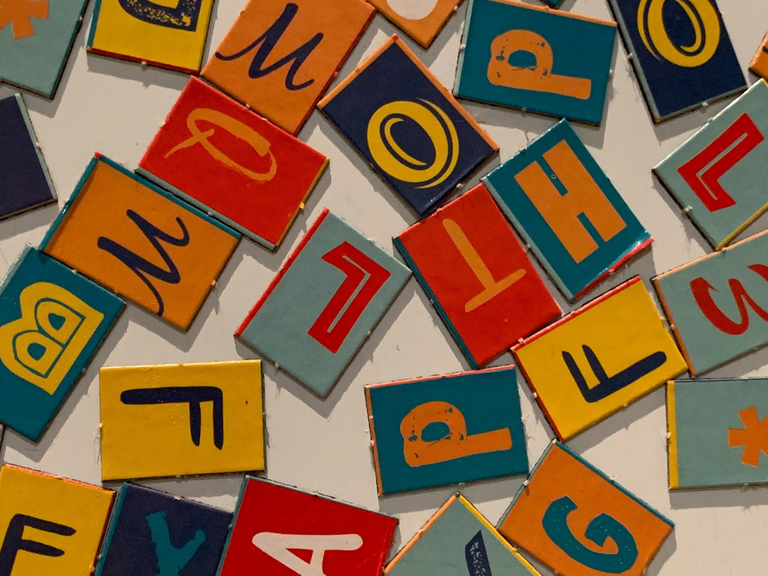 Viele bunte Buchstaben auf Holzstücken liegen durcheinander auf einem weißen Untergrund.