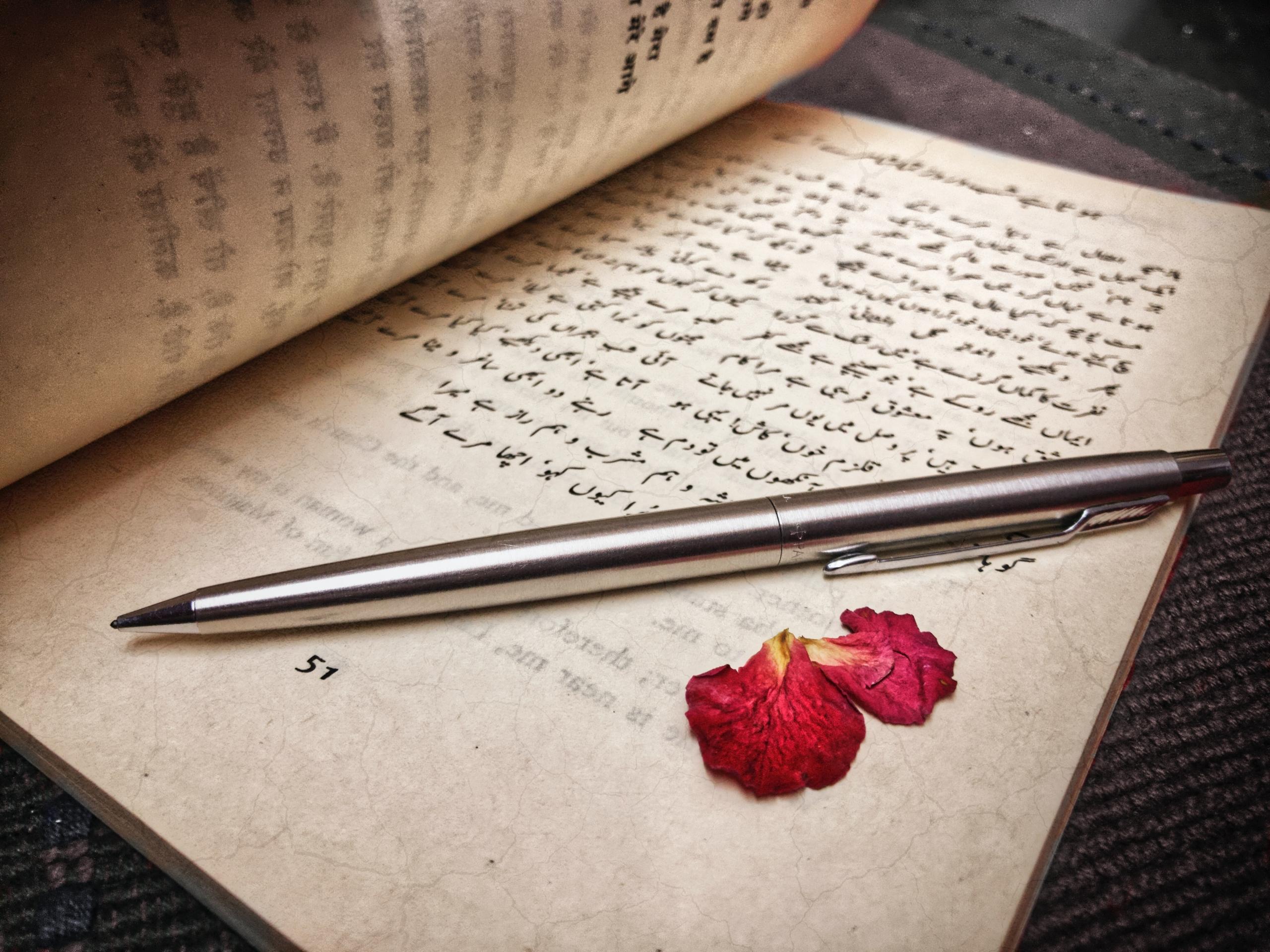 Auf einer Seite mit einem auf Urdu geschriebenen Text liegen Rosenblätter und ein Kugelschreiber.