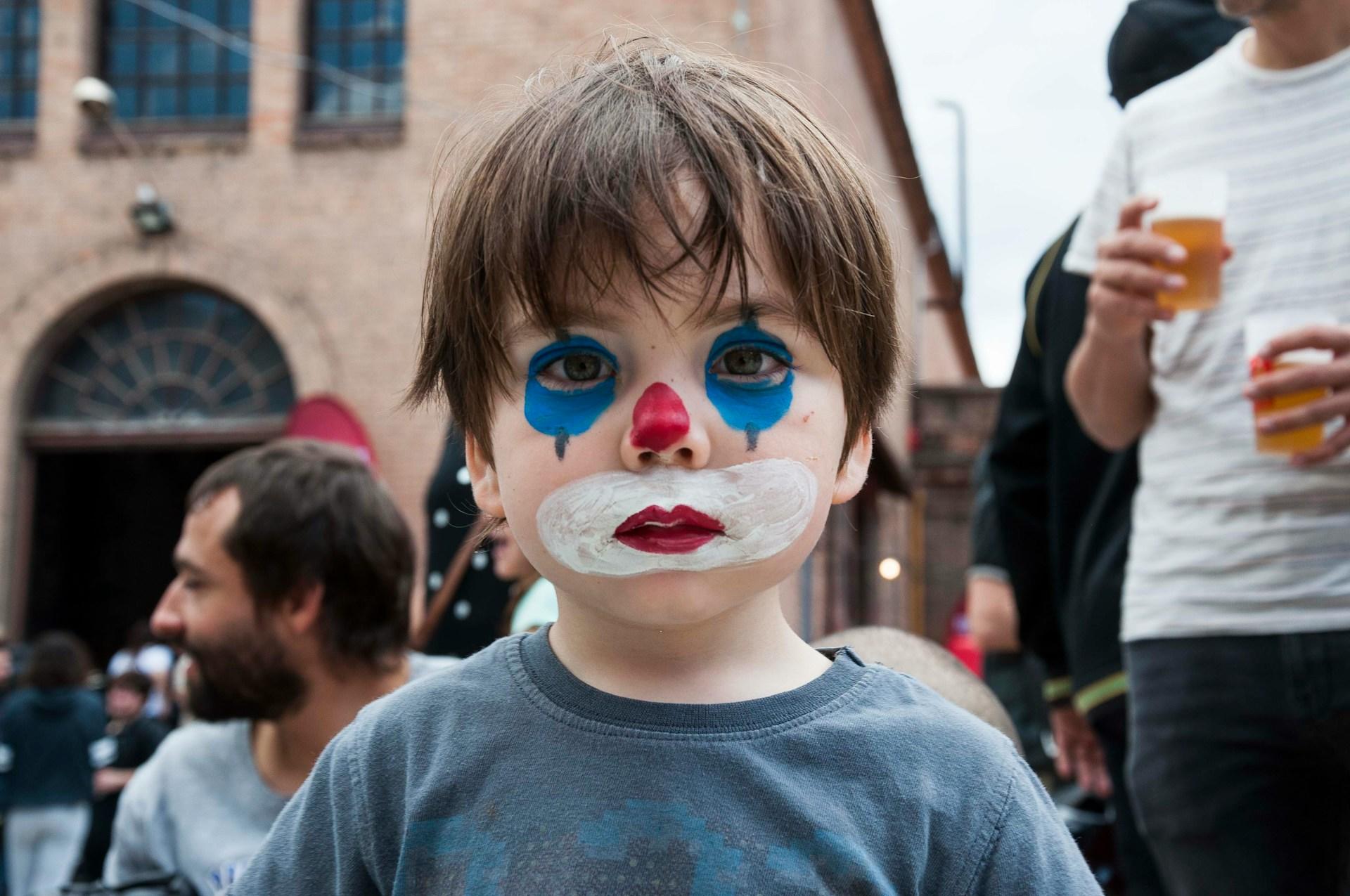 Kinder schminken sich gern wie dieser Junge der als Clown in die Kamera schaut.