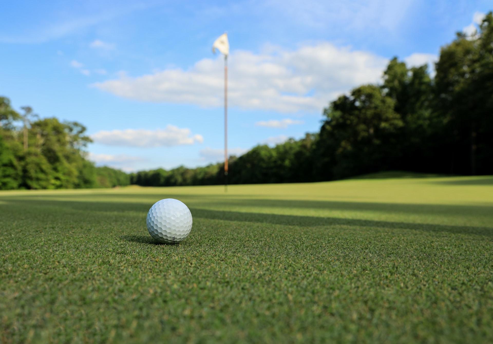 Ein kleiner weißer Golfball liegt auf dem Rasen einige Meter vor dem Loch