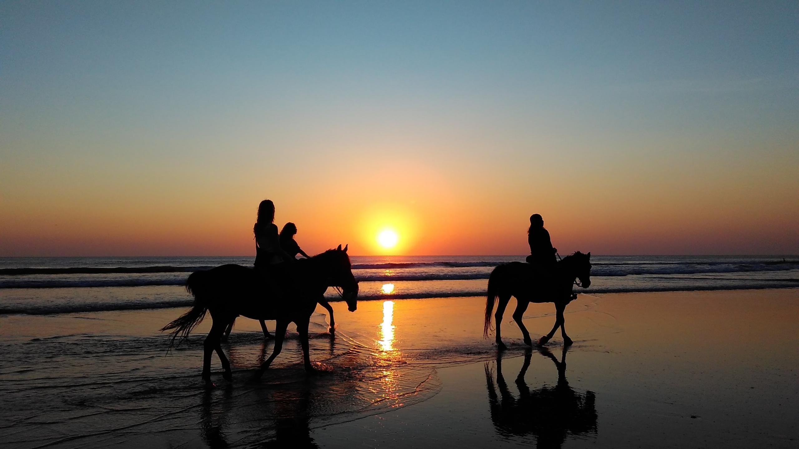 Drei Reiter reiten am Strand zum Sonnenuntergang aus