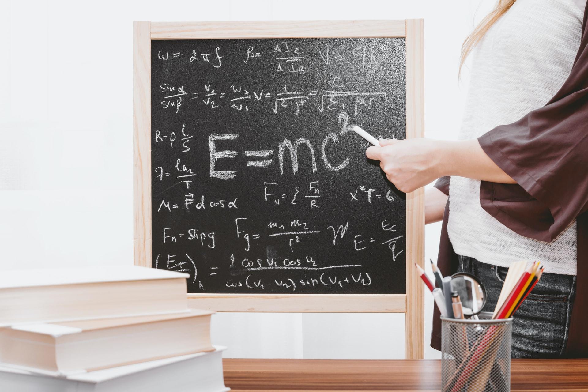 Eine Frau mit Kreide in der Hand steht neben einer Tafel und schreibt die Relativitätstheorie auf.