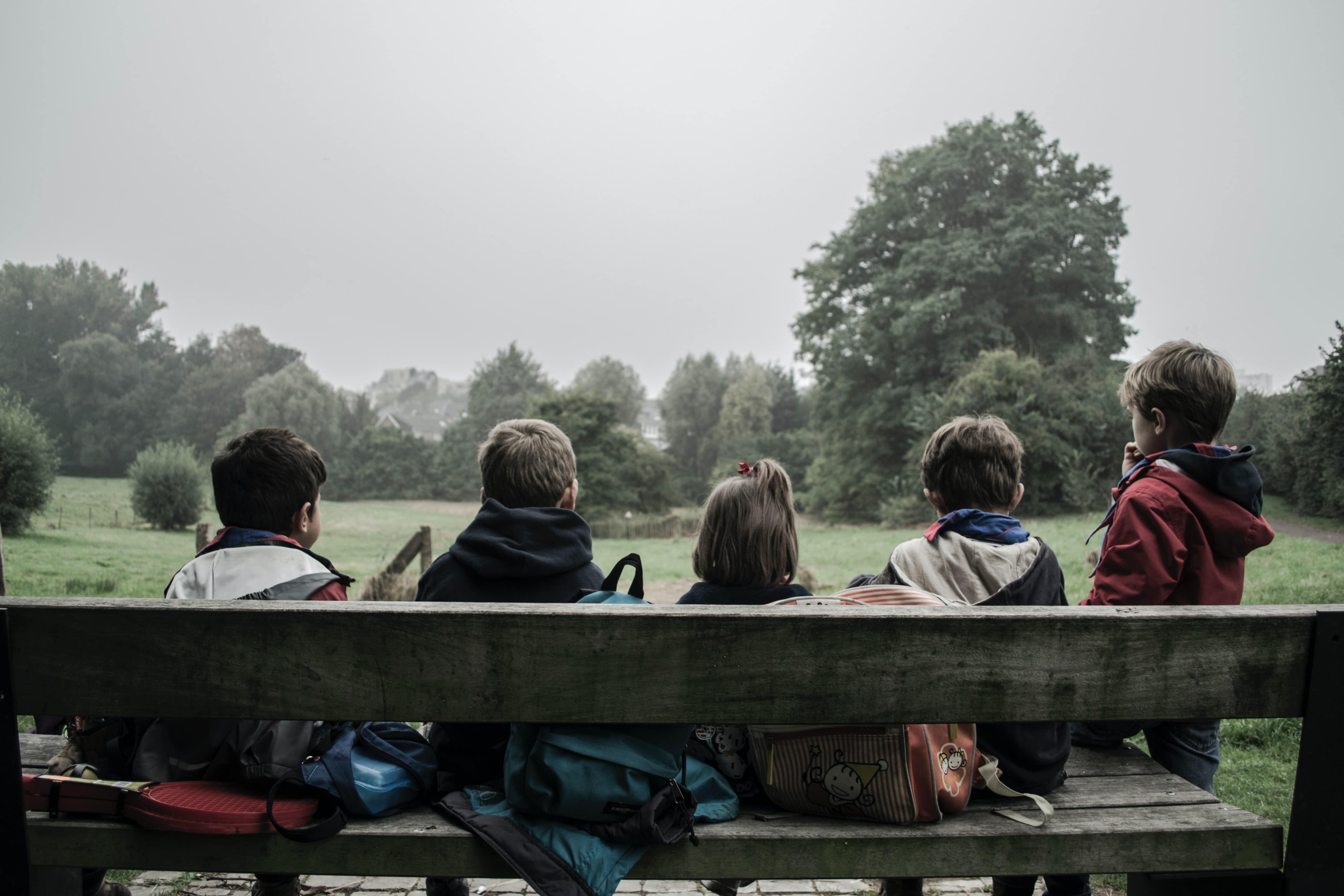 Mehrere Kinder sitzen mit ihren Rucksäcken auf einer Bank und schauen in die Landschaft.