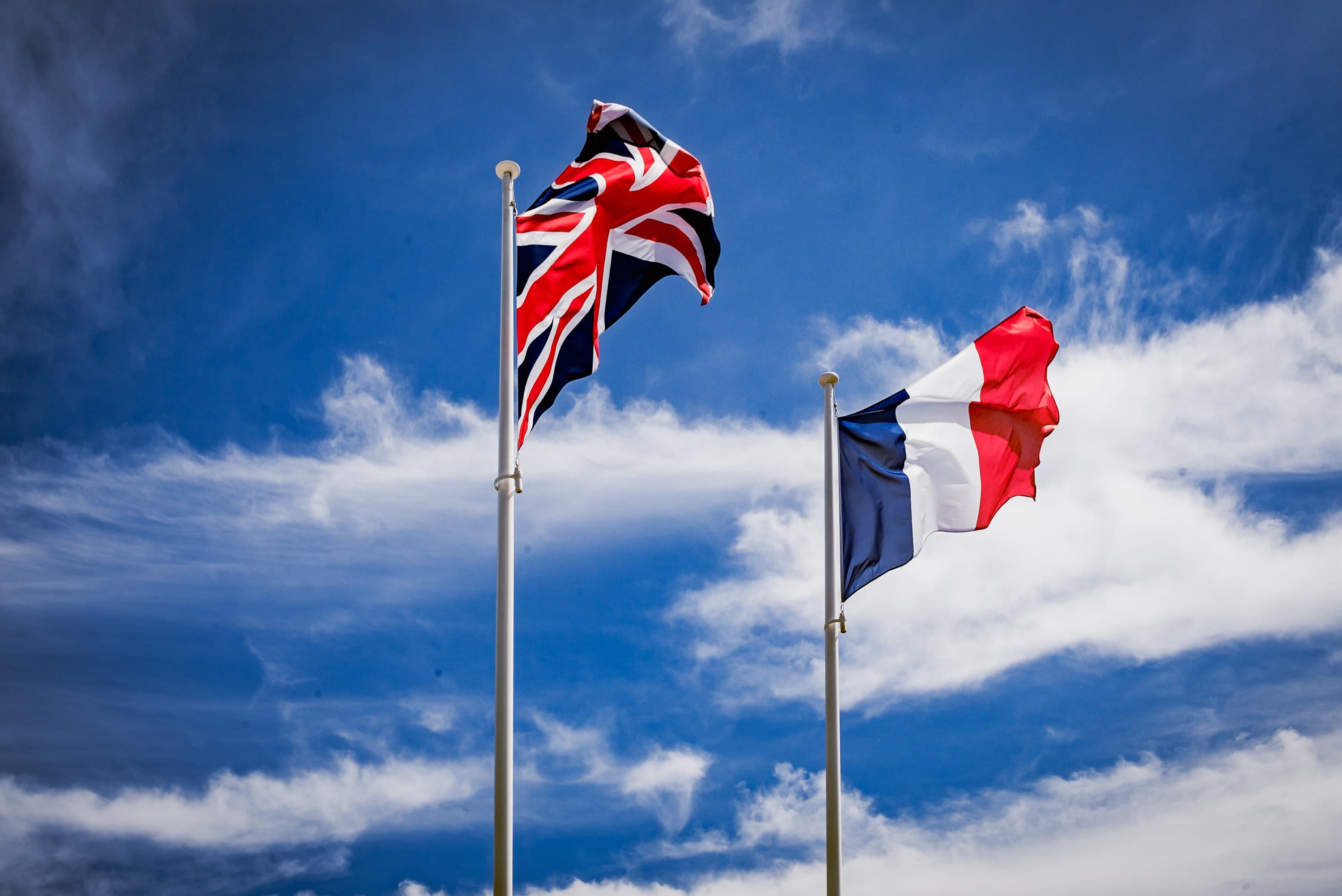 Vor dem blauen Himmel wehen die britische und die französische Flagge im Wind.