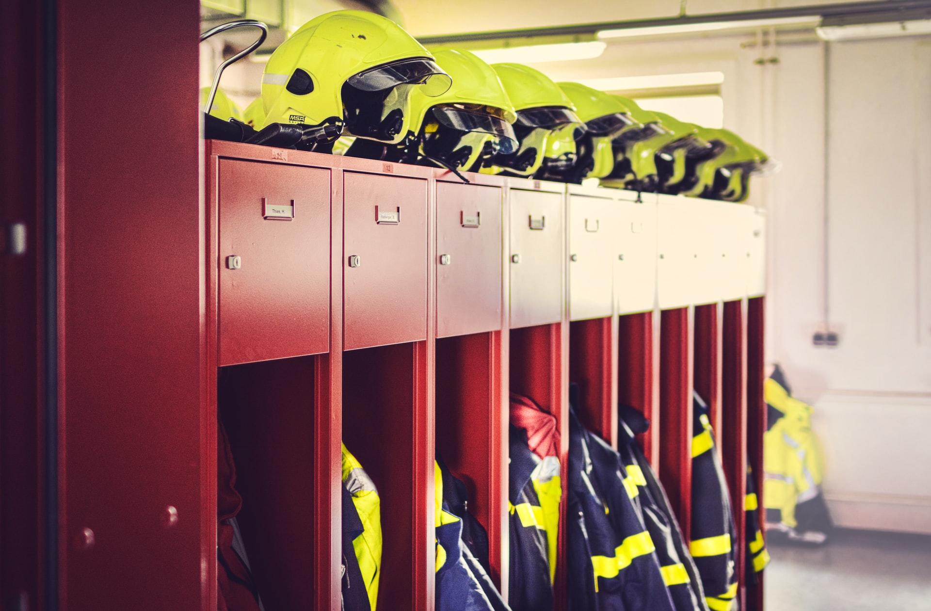 Ein rotes Regal ist gefüllt mit Feuerwehrkleidung, darauf gelbe Feierwehrhelme platziert.