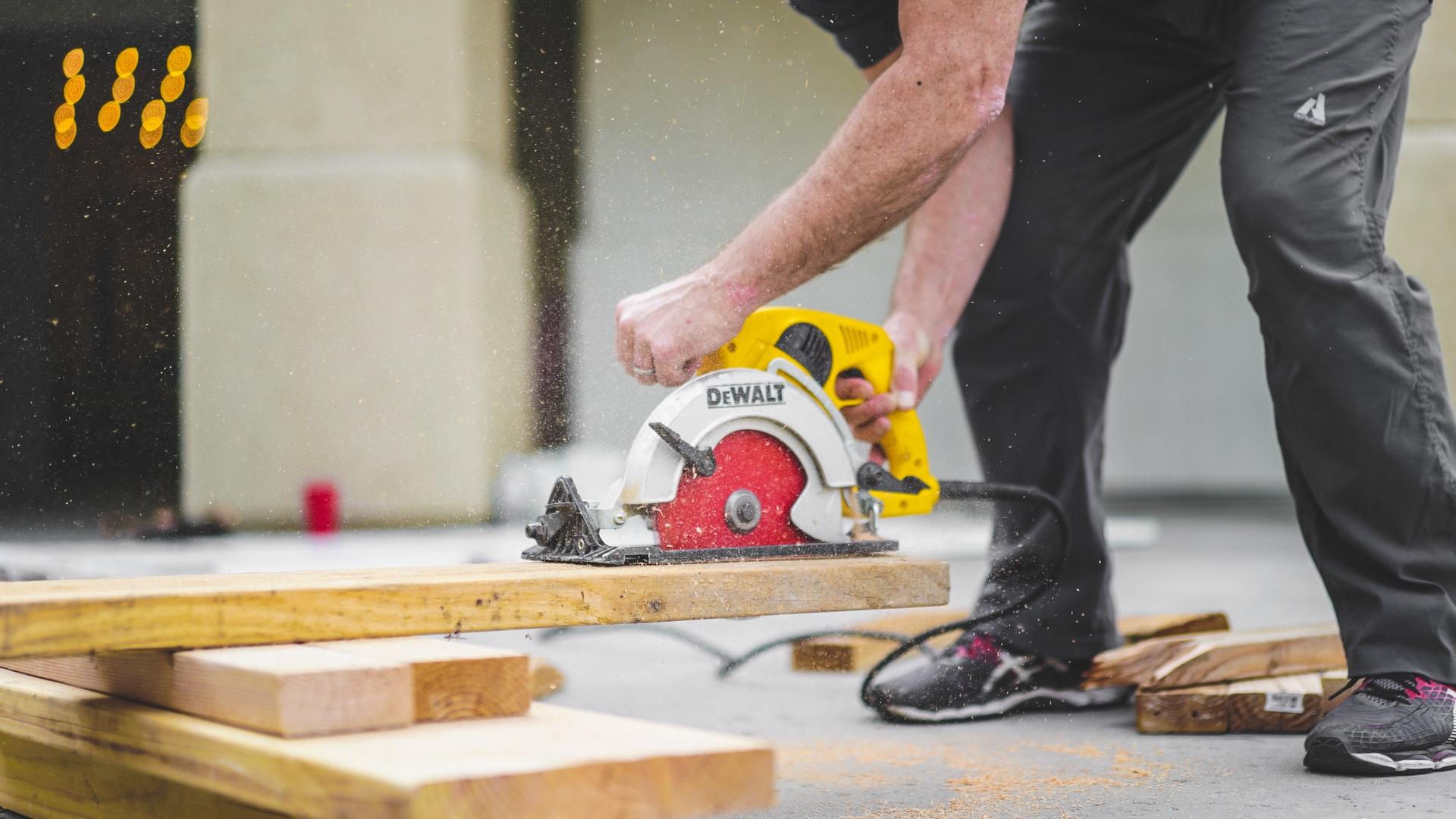Ein Mann hält eine elektrische Säge in der Hand und beugt sich über einen Holzbalken.