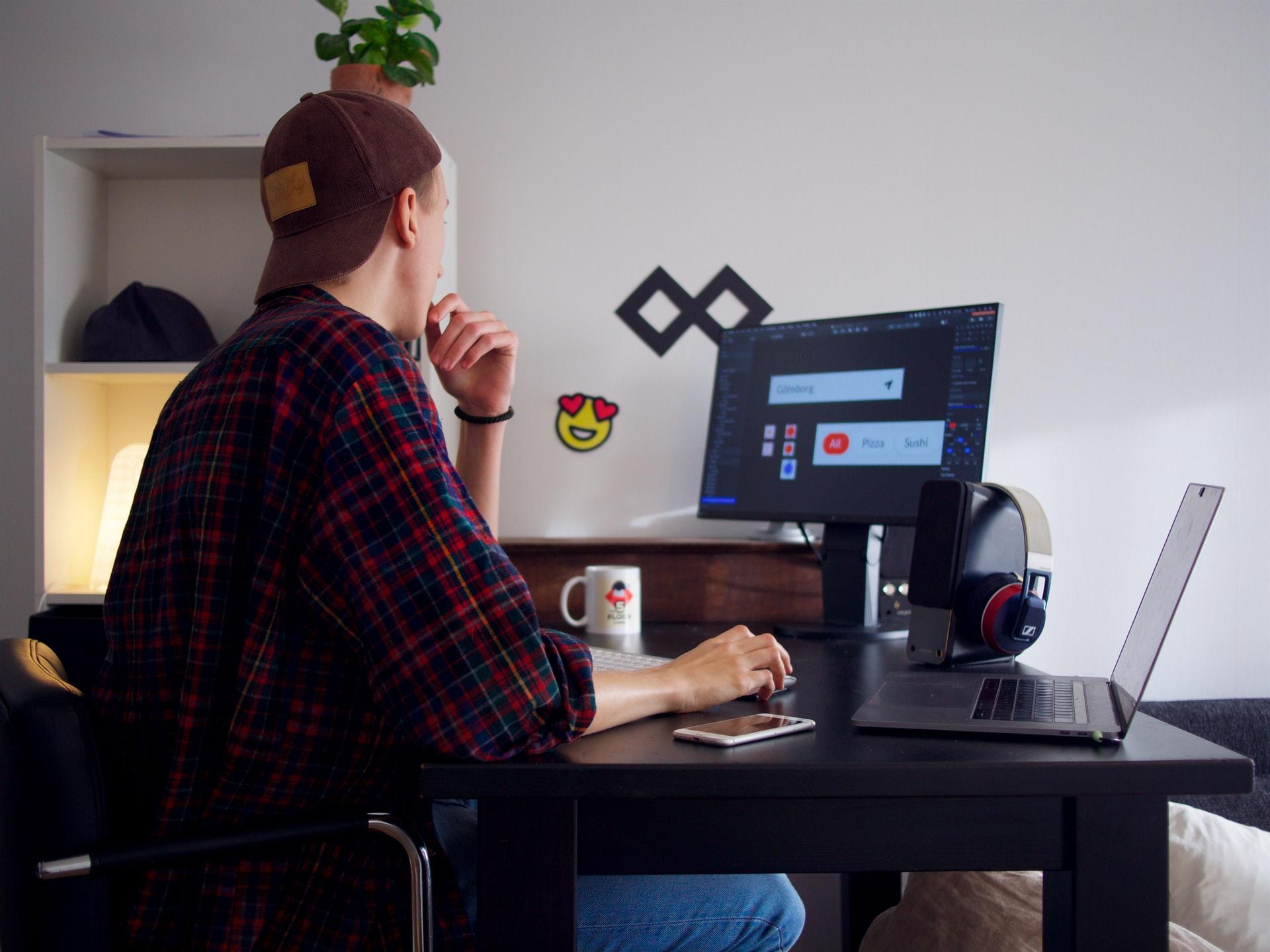 Ein Mann mit Cap sitzt am Schreibtisch und arbeitet am Computer.