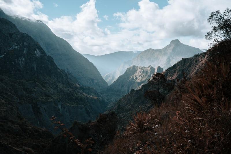 Blick über ein Tal auf La Réunion, in der Ferne sind weitere Berge.