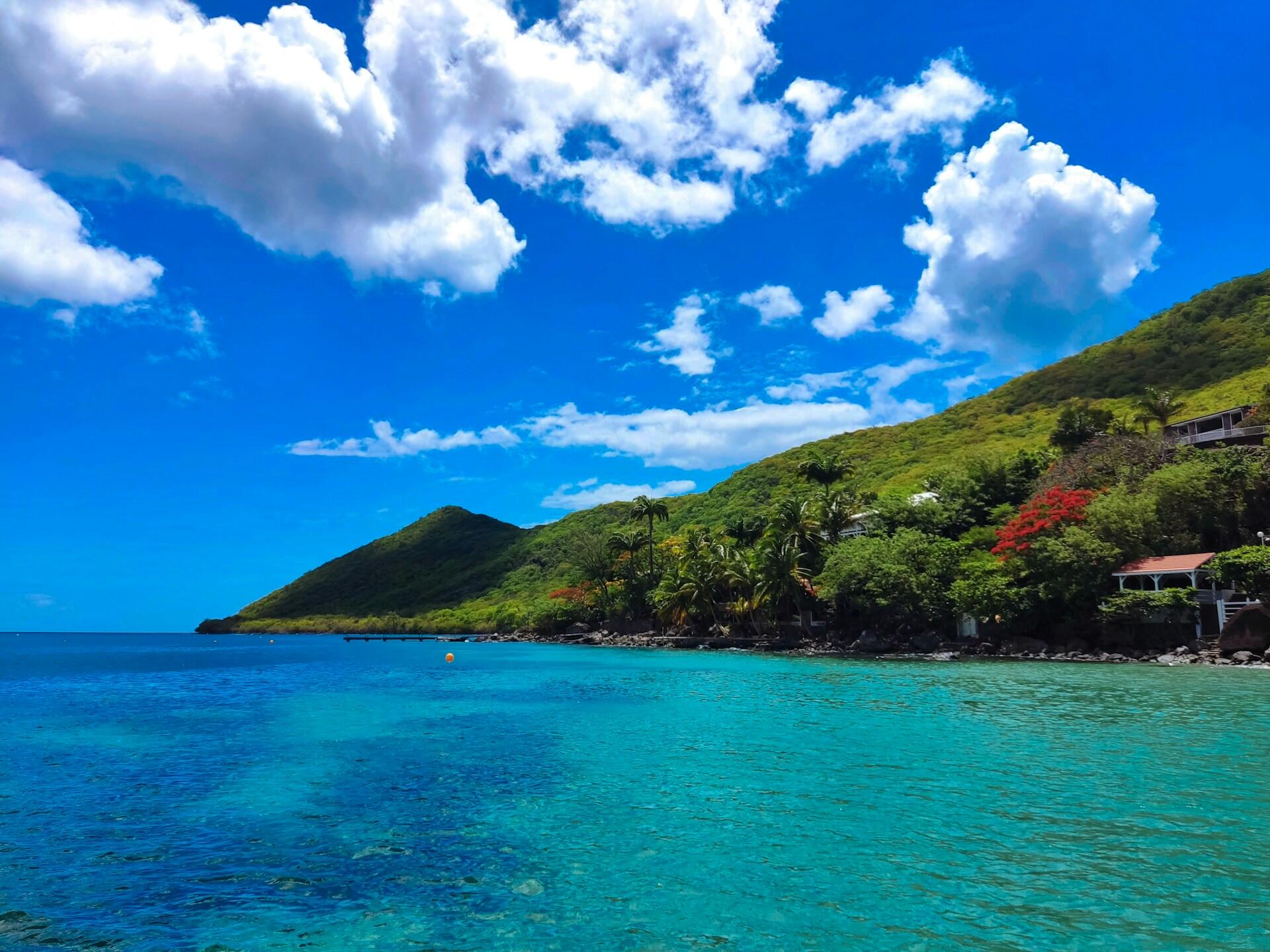 Insel mit grünen Hügeln vor blauem Meer und Himmel mit Wolken.