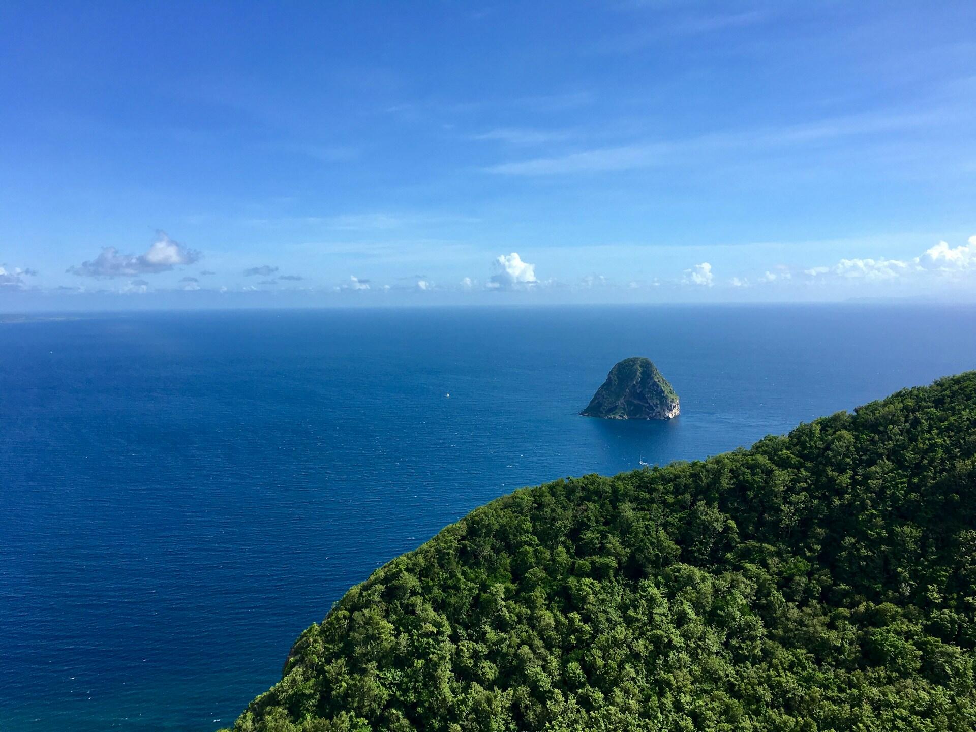 Insel mit Bäumen mit Klippe vor blauem Meer.