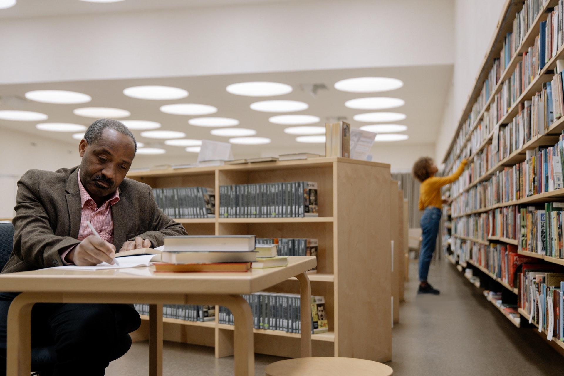 Mann mit Stift und Büchern in einer Universitätsbibliothek
