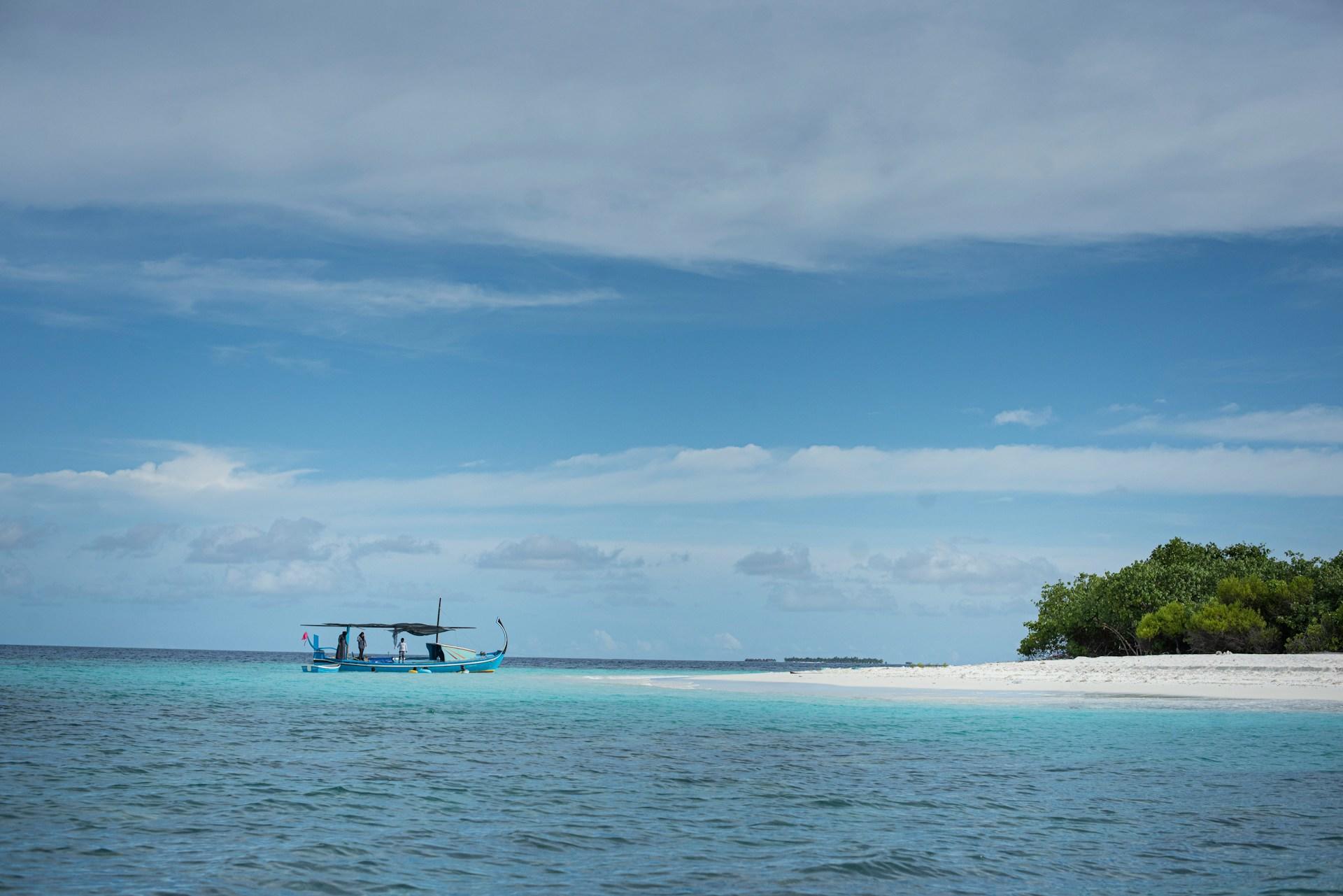 Ein Boot im türkisblauen Meer vor einem weißen Sandstrand mit Palmen und darüber der blaue Himmel.