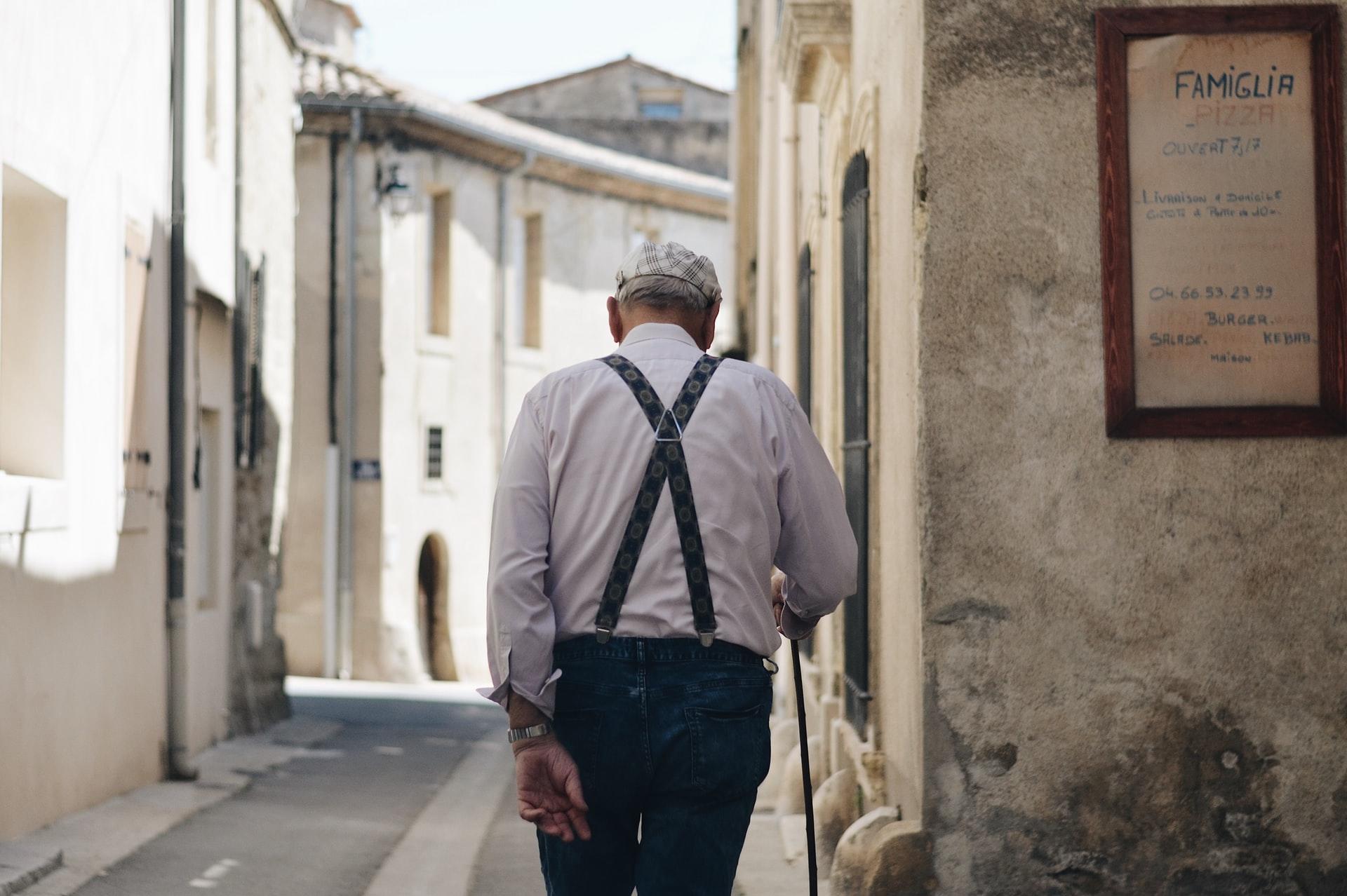 Ein Mann mit Gehstock läuft durch eine alte schmale Gasse.