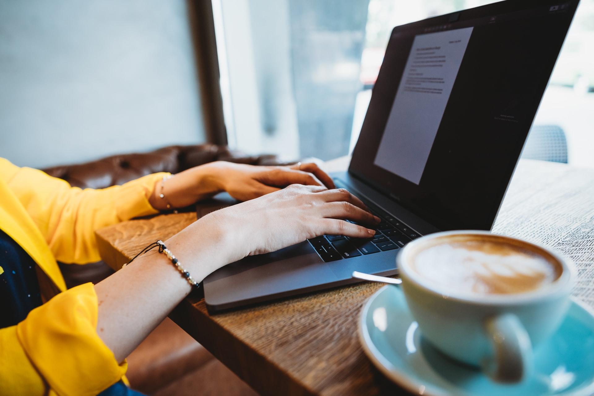 Eine Person nutzt einen Laptop auf einem Tisch und daneben steht eine Kaffeetasse.