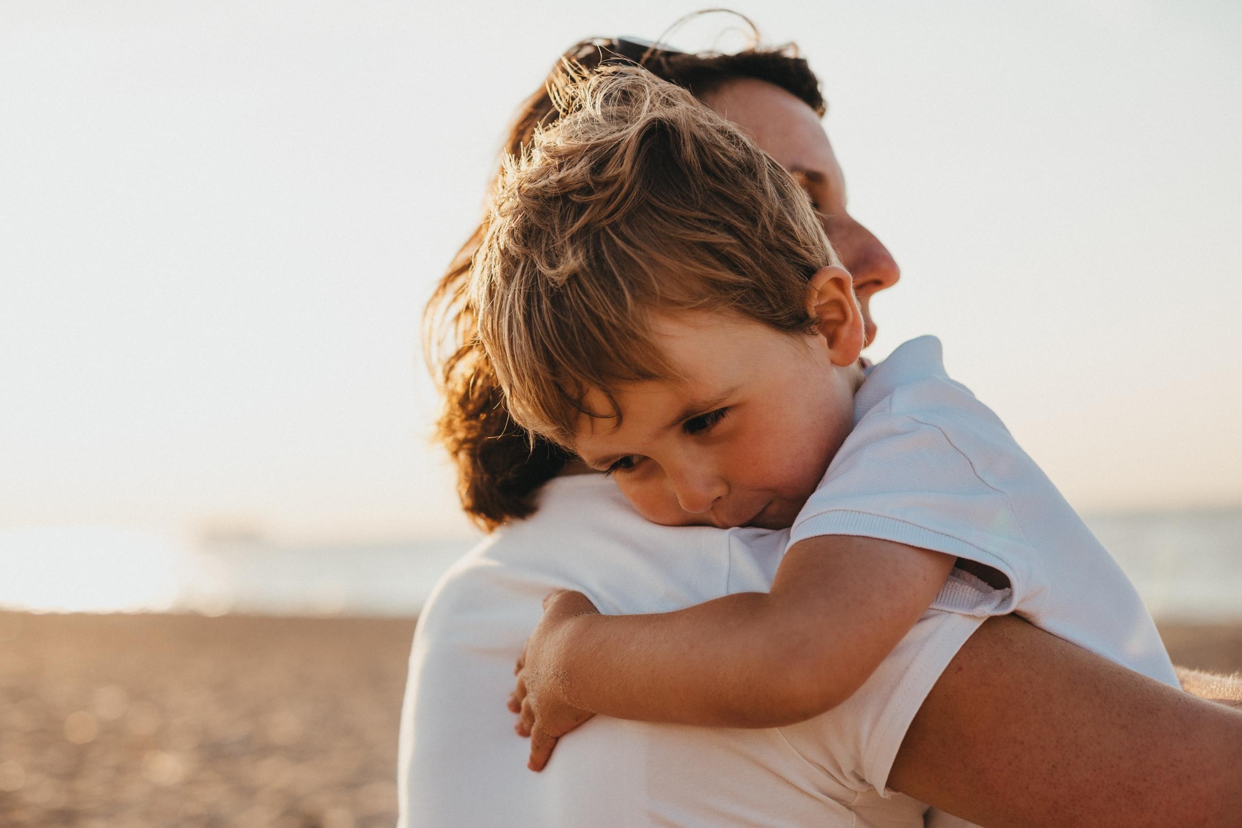 Am Strand hält sein Vater seinen Jungen im Arm. Viele Kinder denken schon in den Sommerferien an die bevorstehende Einschulung.