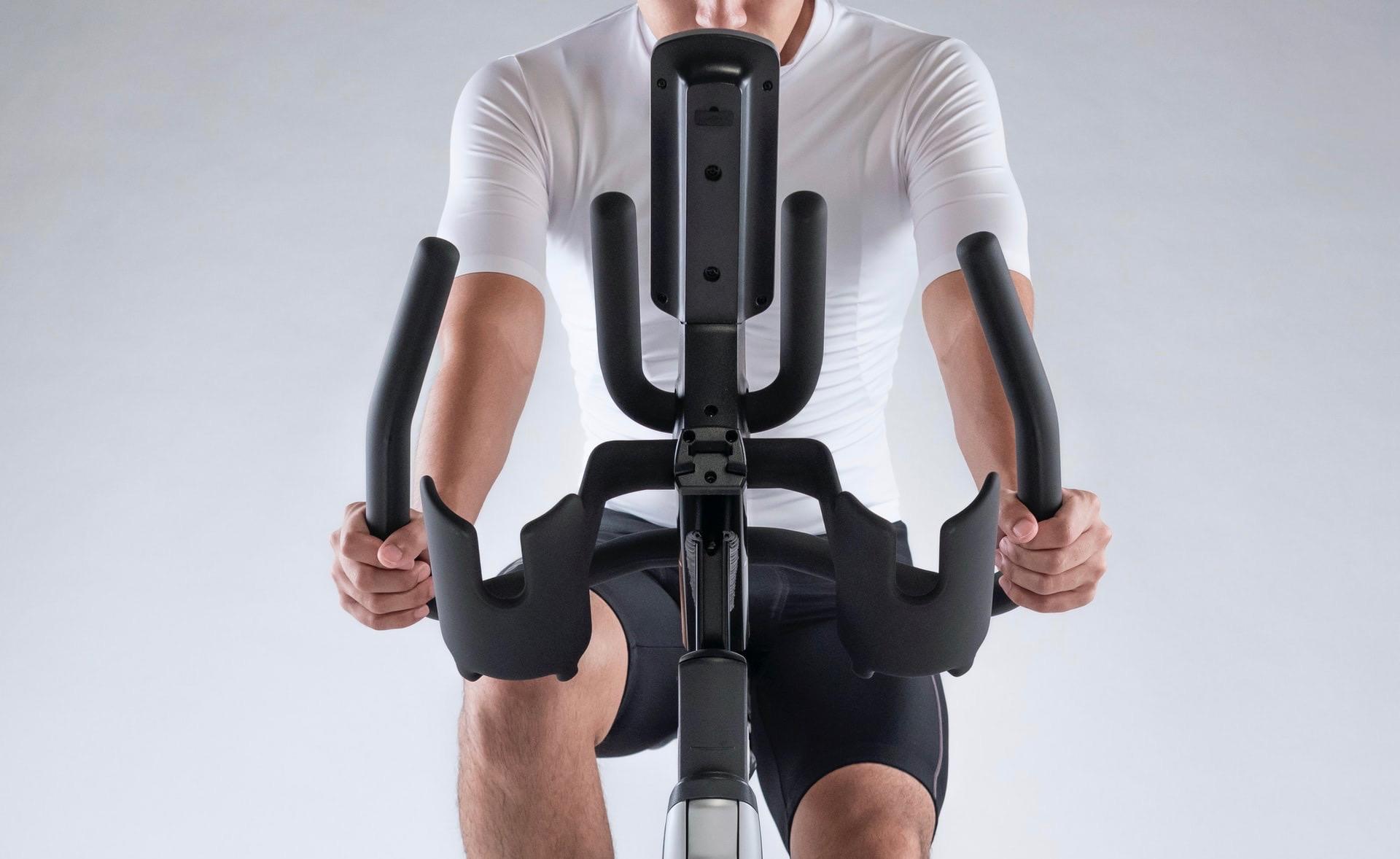 Dieser junge Mann mit weißem T-Shirt von vorne auf einem Ergometer fotografiert behält seine Fitness mit regelmäßigem Training