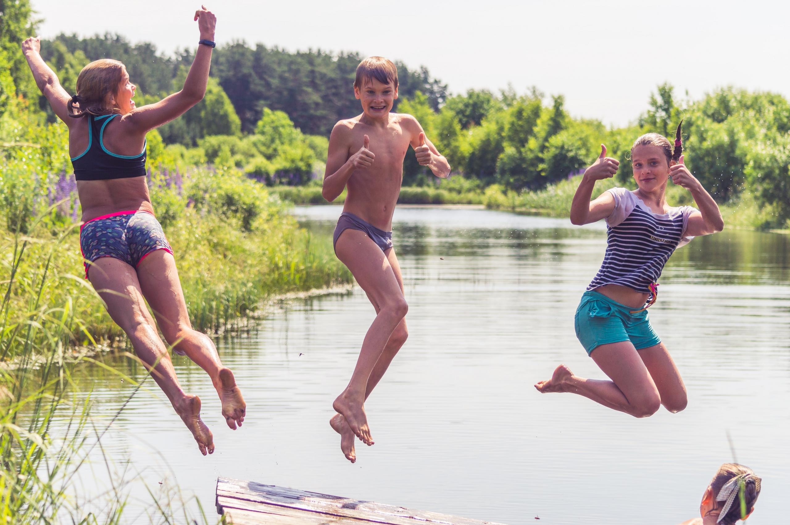 Drei grosse Kinder springen Faxen machend in einen See.