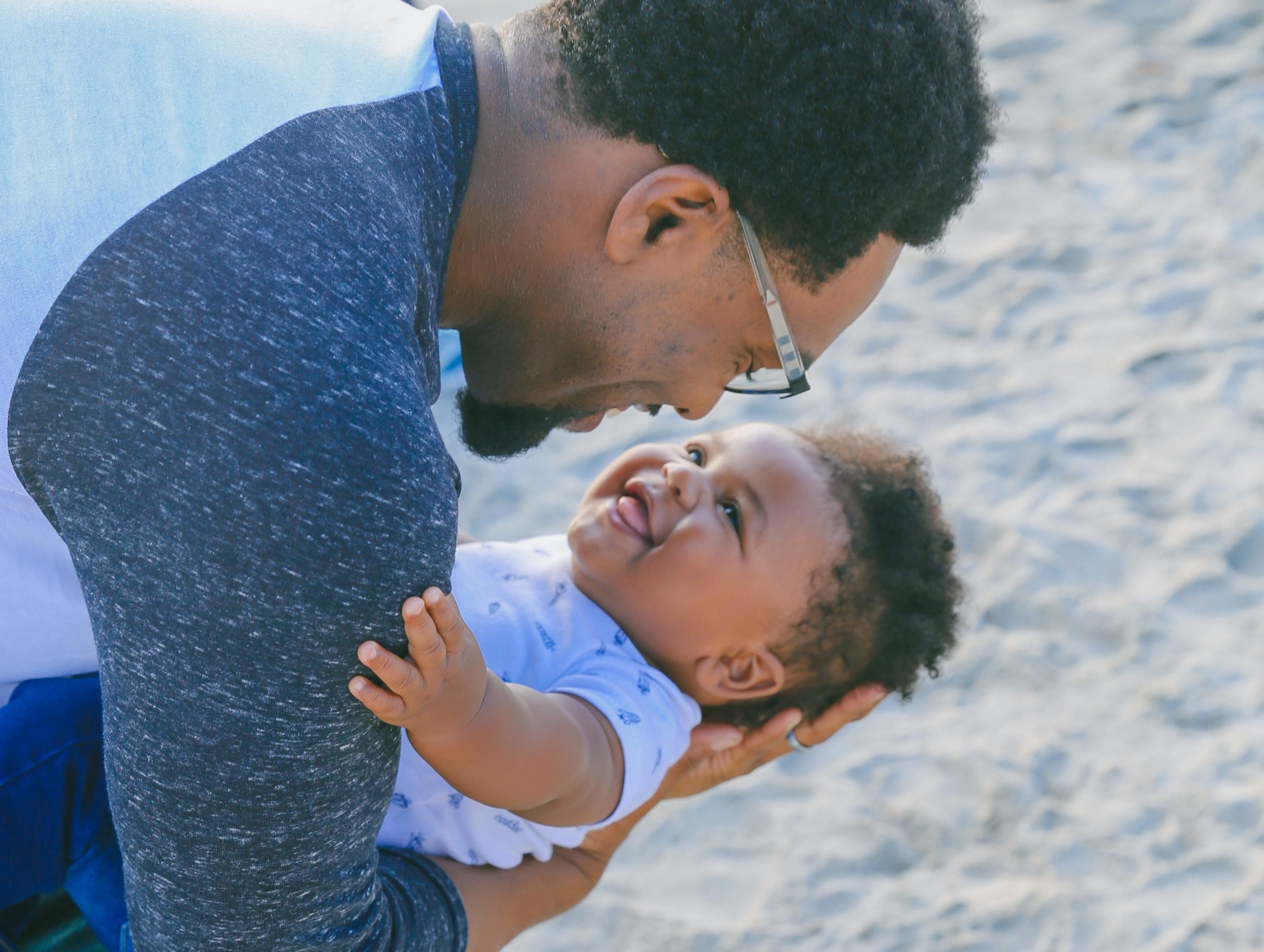 Am Strand hält ein Vater sein lachendes Baby im Arm. 
