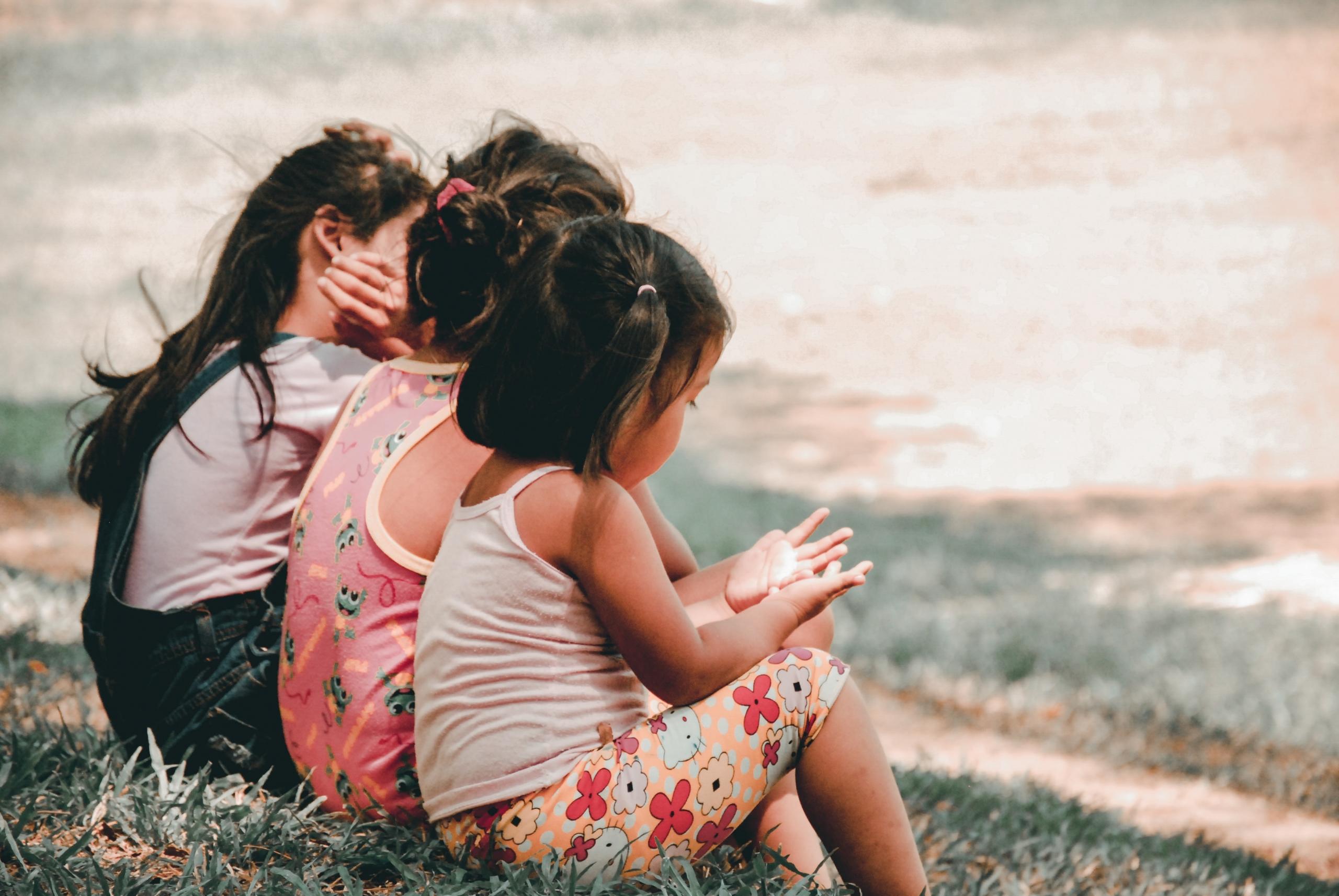 Drei kleine Kinder sitzen nebeneinander auf einer Wiese.