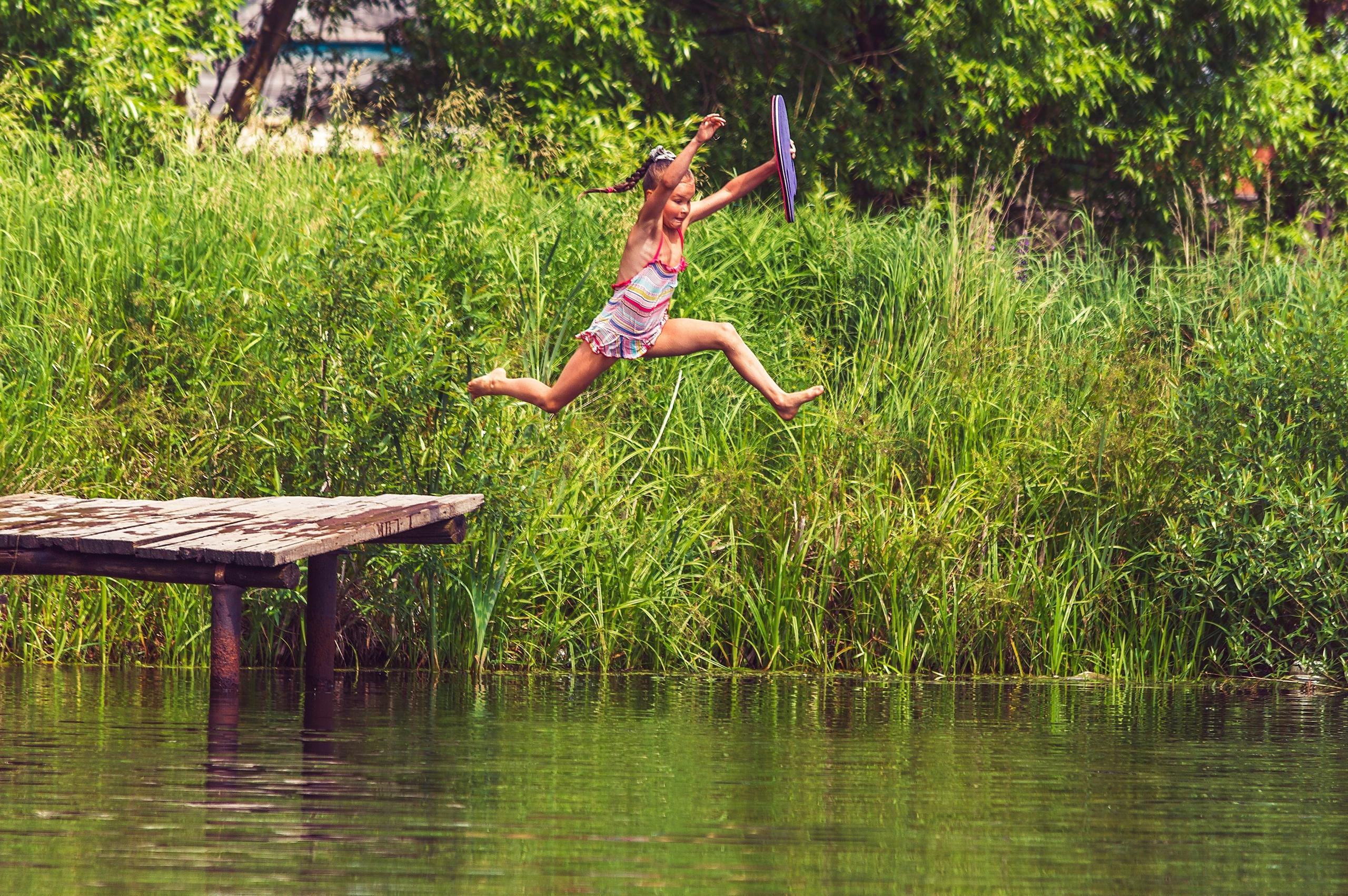 Ein Mädchen springt mit Anlauf von einem Steg ins Wasser eines Sees. 